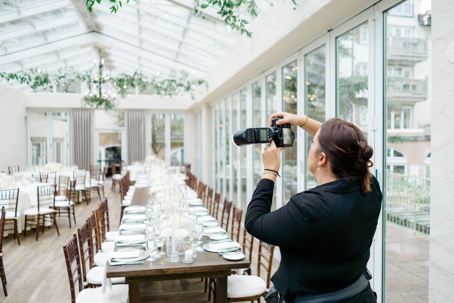 Vail Photographer capturing elegant wedding reception table setup in a bright greenhouse venue with white chairs and long dining tables.