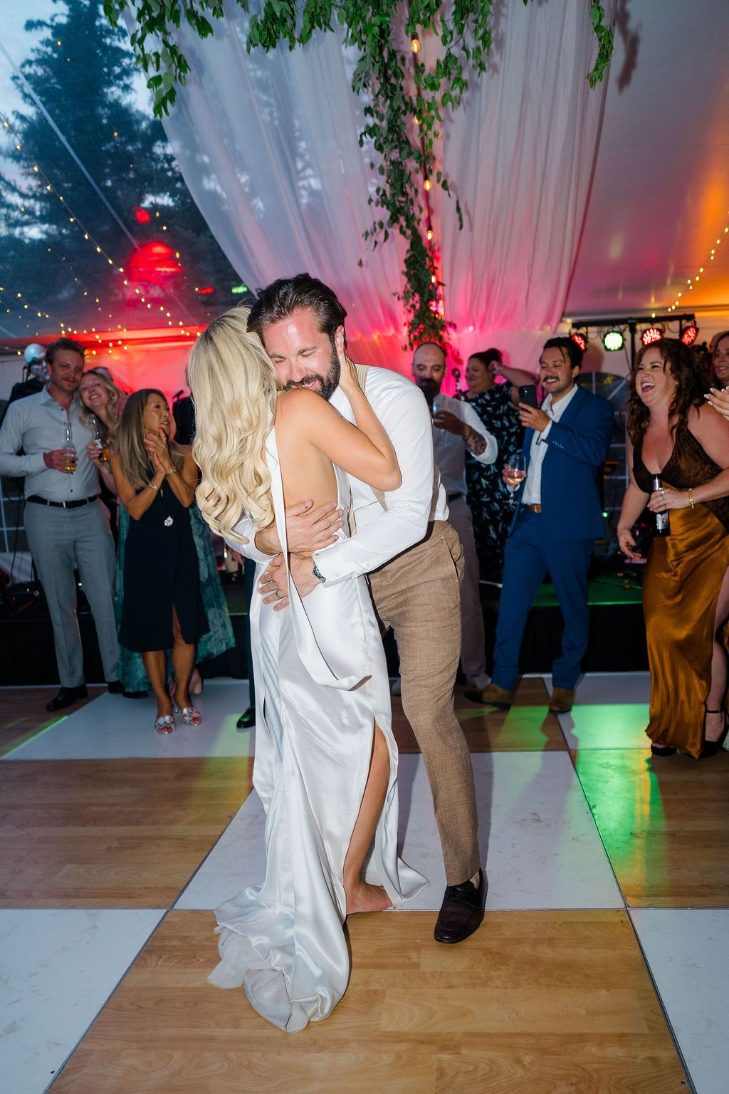 Bride and groom share romantic first dance embrace under draped tent with string lights at wedding reception.
