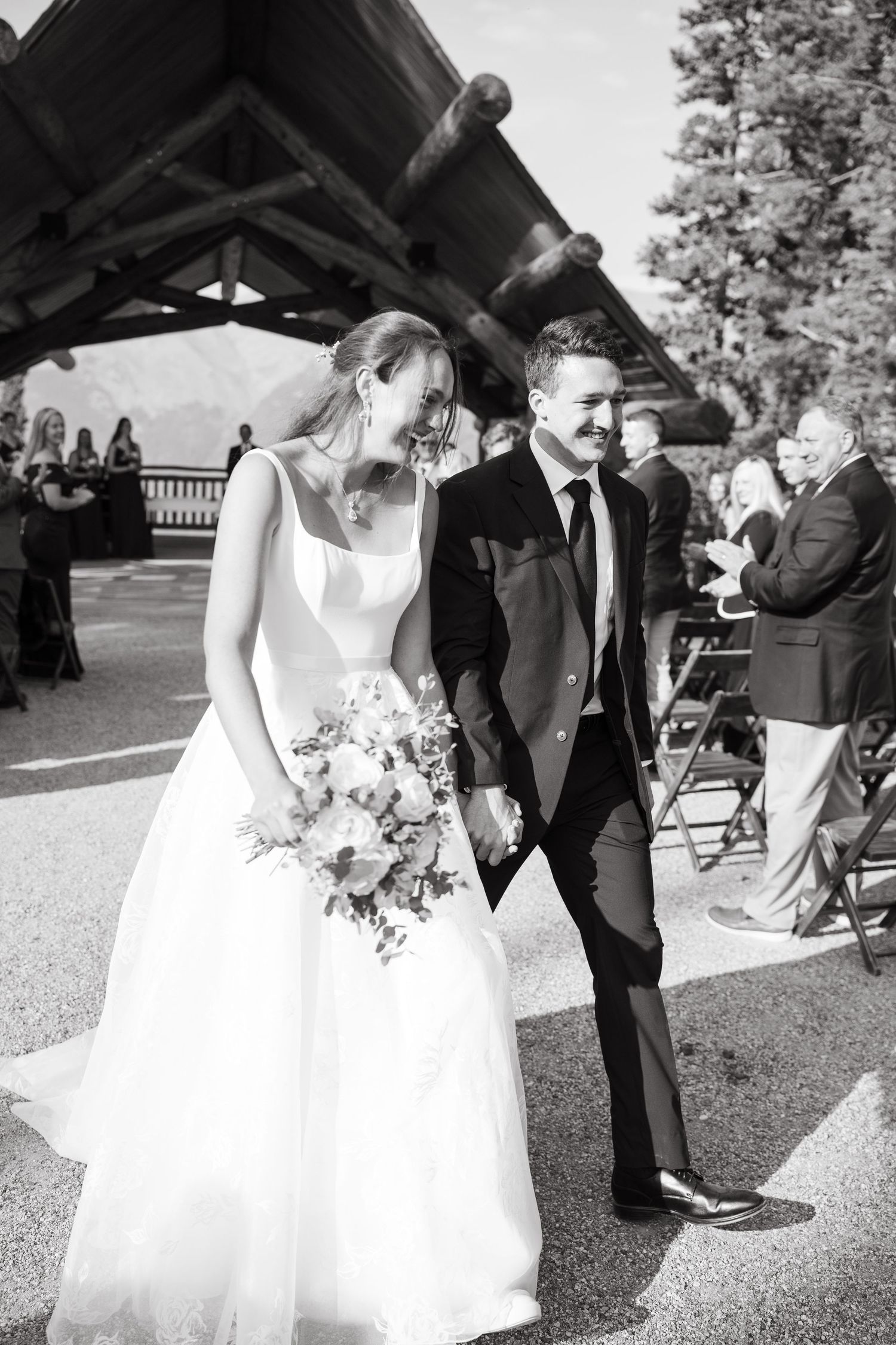 A black and white wedding photo showing a couple walking together outdoors, with the bride holding a floral bouquet at copper mountain.