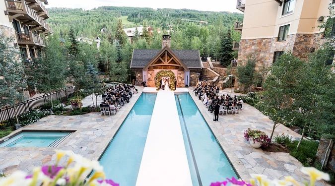 Four Seasons Vail Wedding Elegant outdoor wedding ceremony beside a pool with mountain views and lush forest backdrop at a luxury resort.