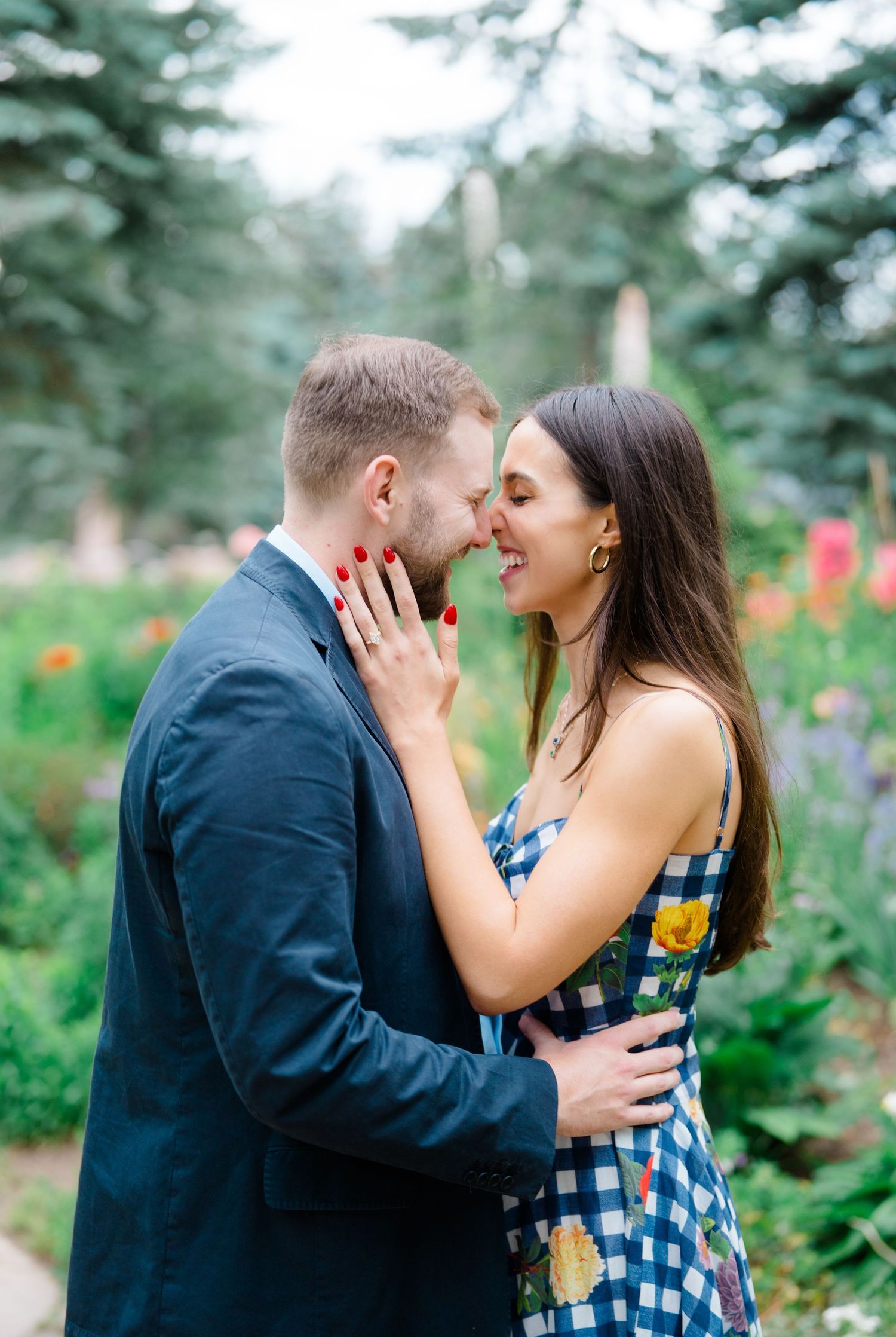 A couple shares intimate moments in a garden setting with blooming flowers and greenery in the background.