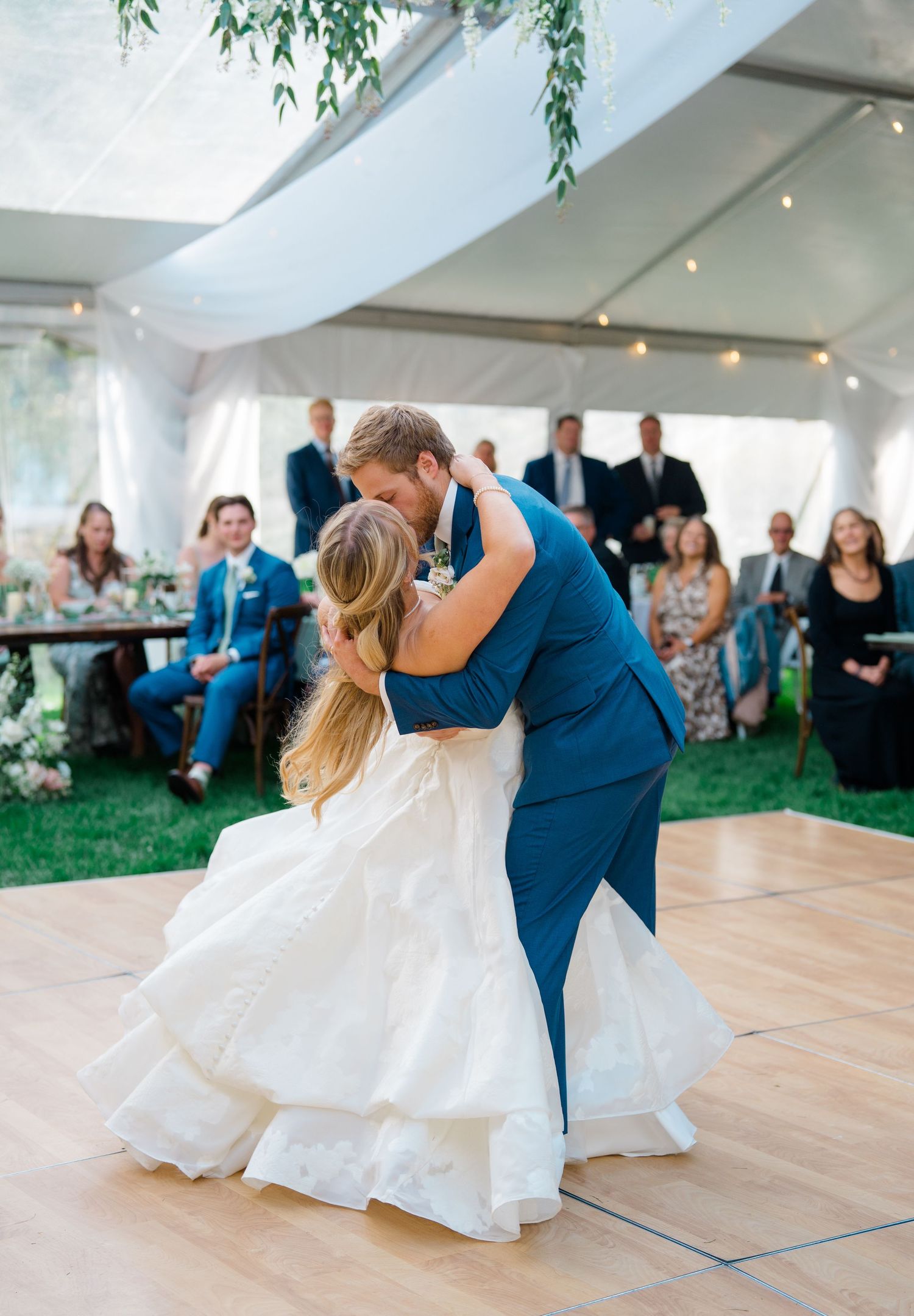Wedding couple dancing under a white tent with guests watching from tables in the background.