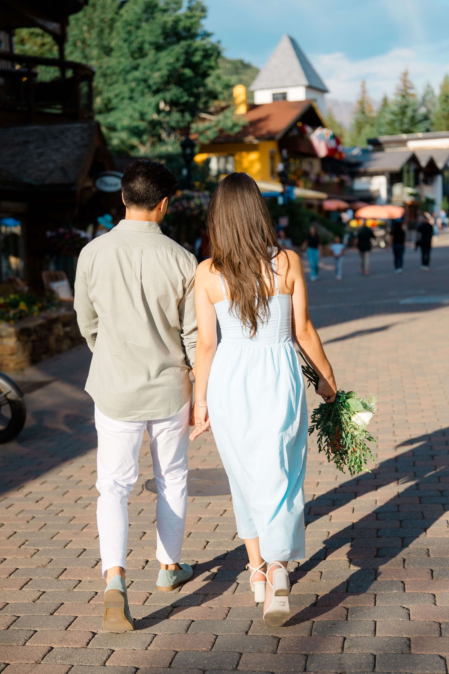 Couple walking together on brick paved path holding hands and carrying fresh flowers after their vail village proposal