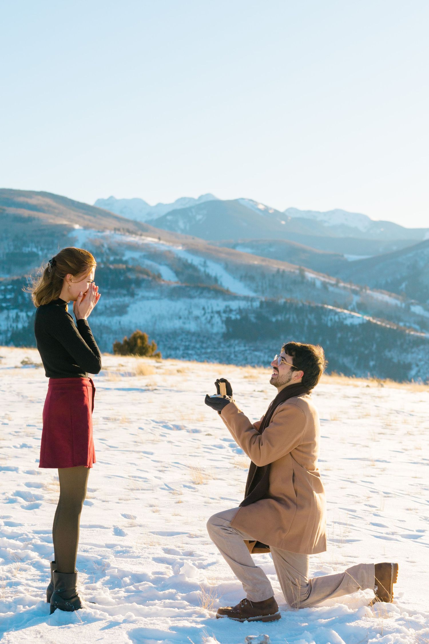 A romantic winter proposal scene unfolds in snowy mountains with a couple silhouetted against the scenic landscape.