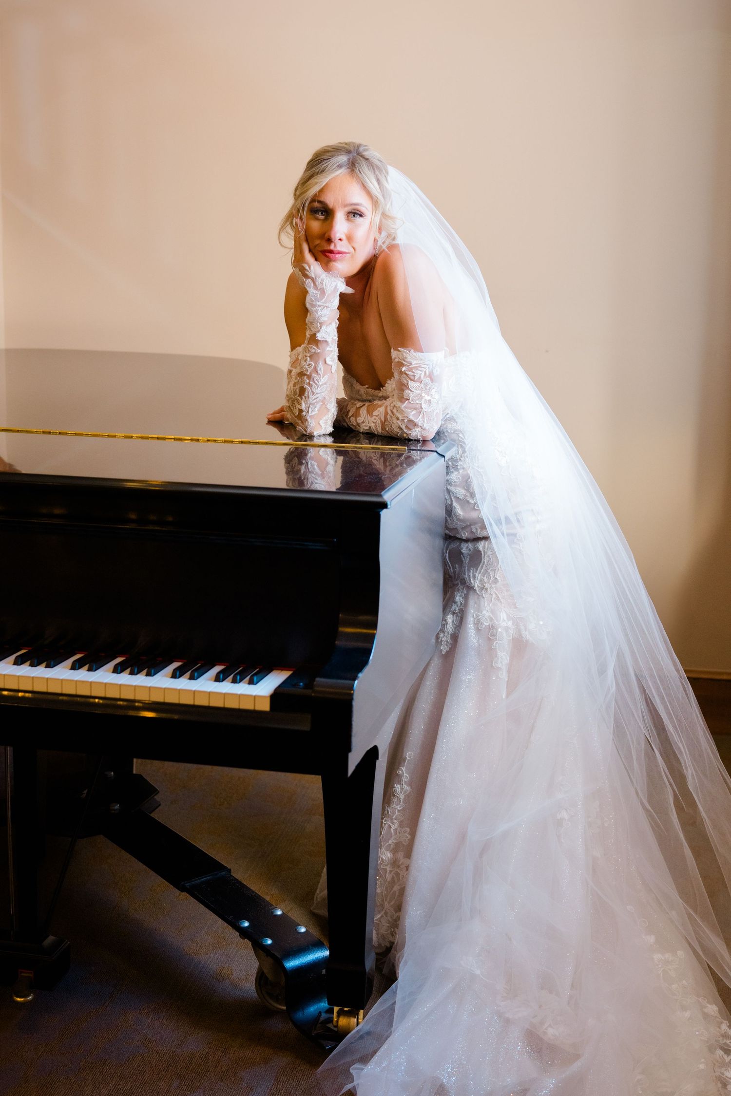 Bride in white lace gown poses elegantly near a grand piano.
