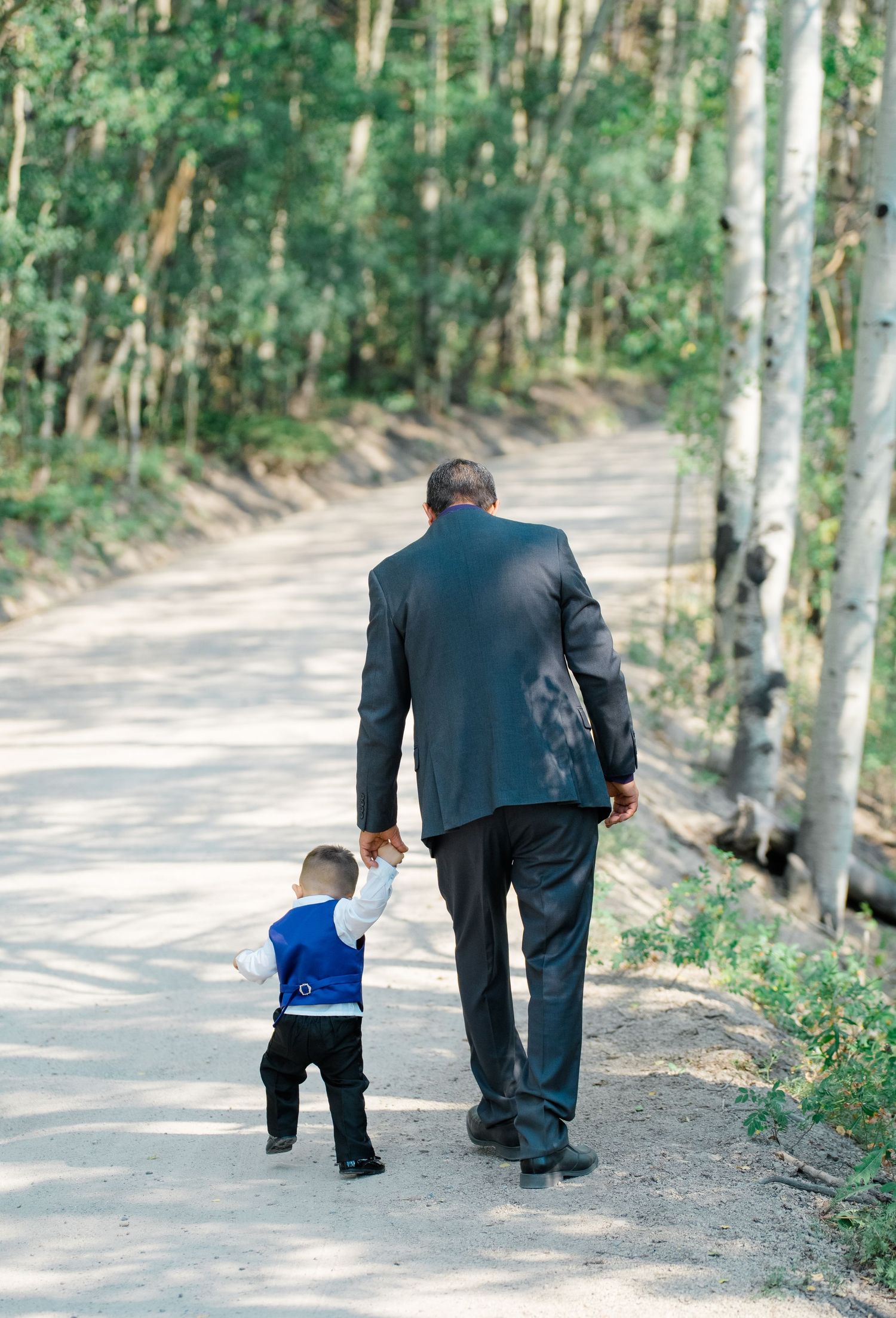 A sequence of images showing a small child and adult walking together down a tree-lined path in formal attire during Breckenridge wedding.