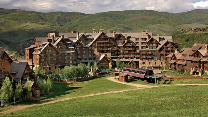 Luxury mountain resort lodge surrounded by lush green hills and manicured grounds in a scenic valley setting.