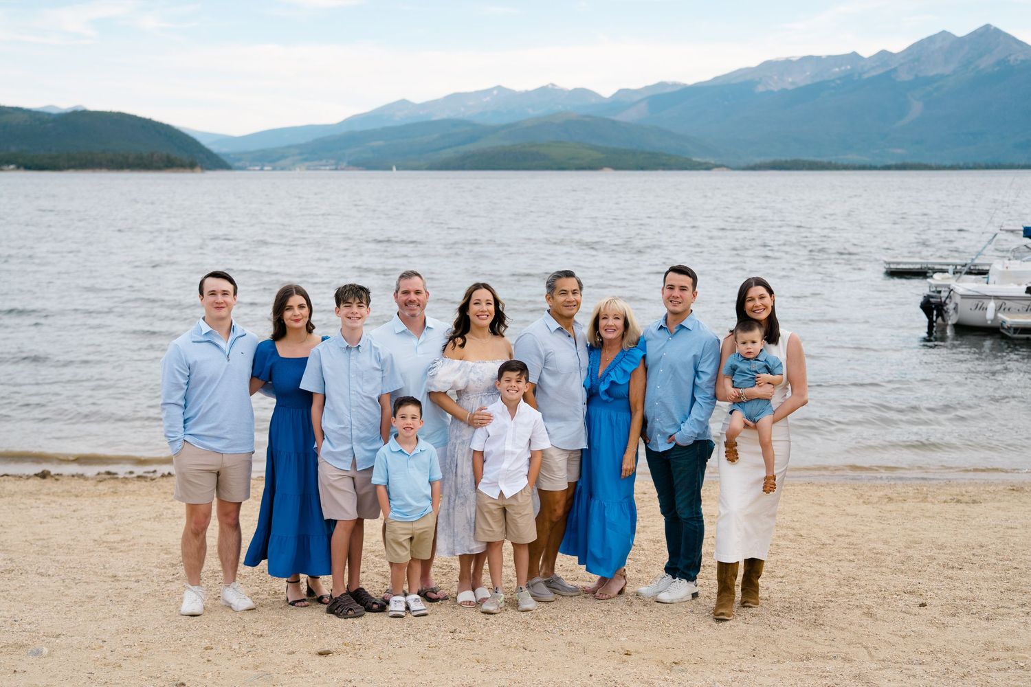 Lake dillon proposal - A group of people pose for photos on a beach with mountains and lake in the background during a sunny day.