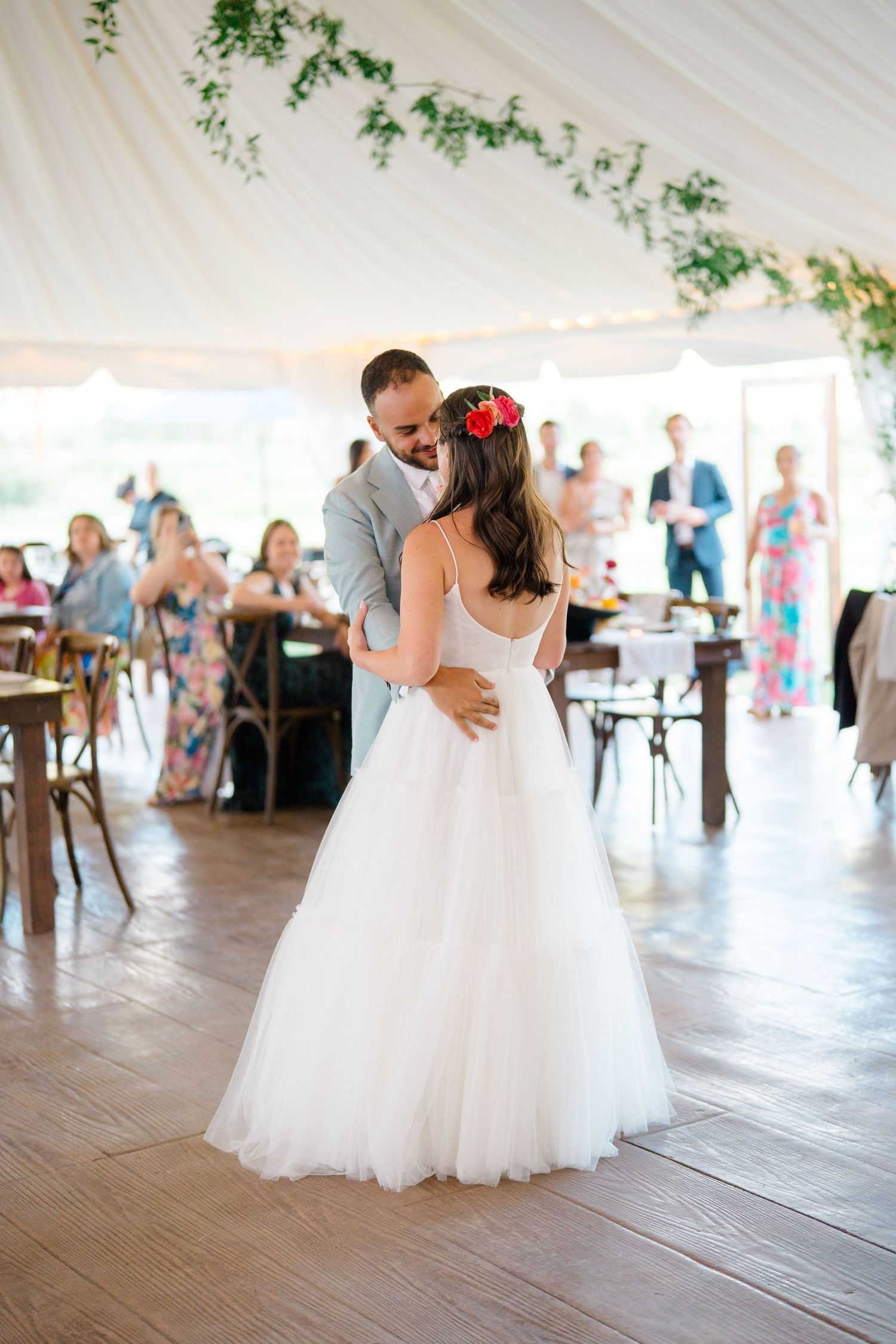Wedding couples dancing under white tent during reception celebration.