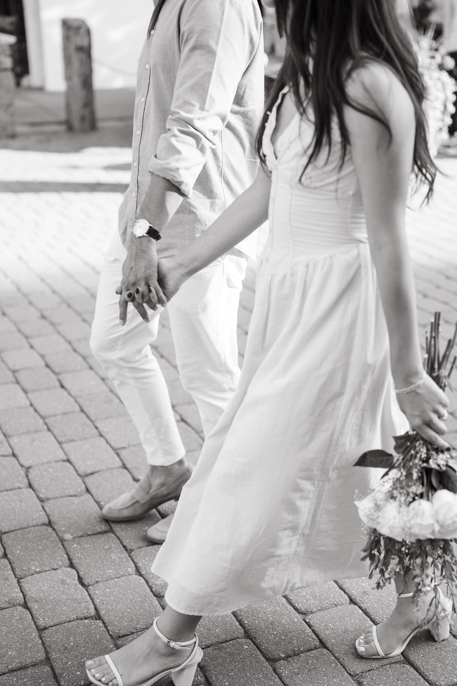 A couple in light summer attire walking together on a brick paved pathway.