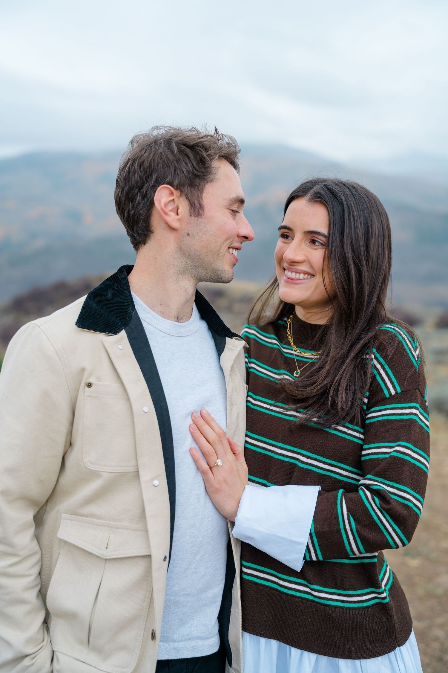 A couple shares tender moments while wearing casual attire against a mountainous backdrop.