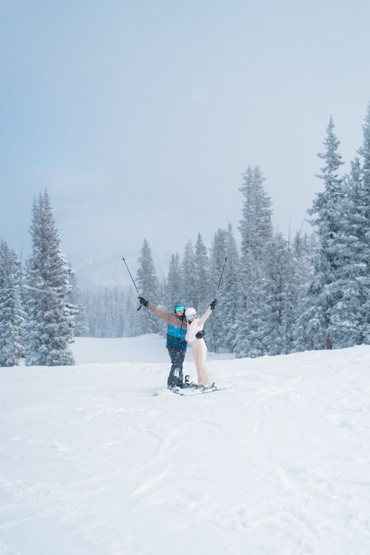 Skiers enjoying fresh powder snow on a mountain slope surrounded by snow-covered evergreen trees in winter conditions.