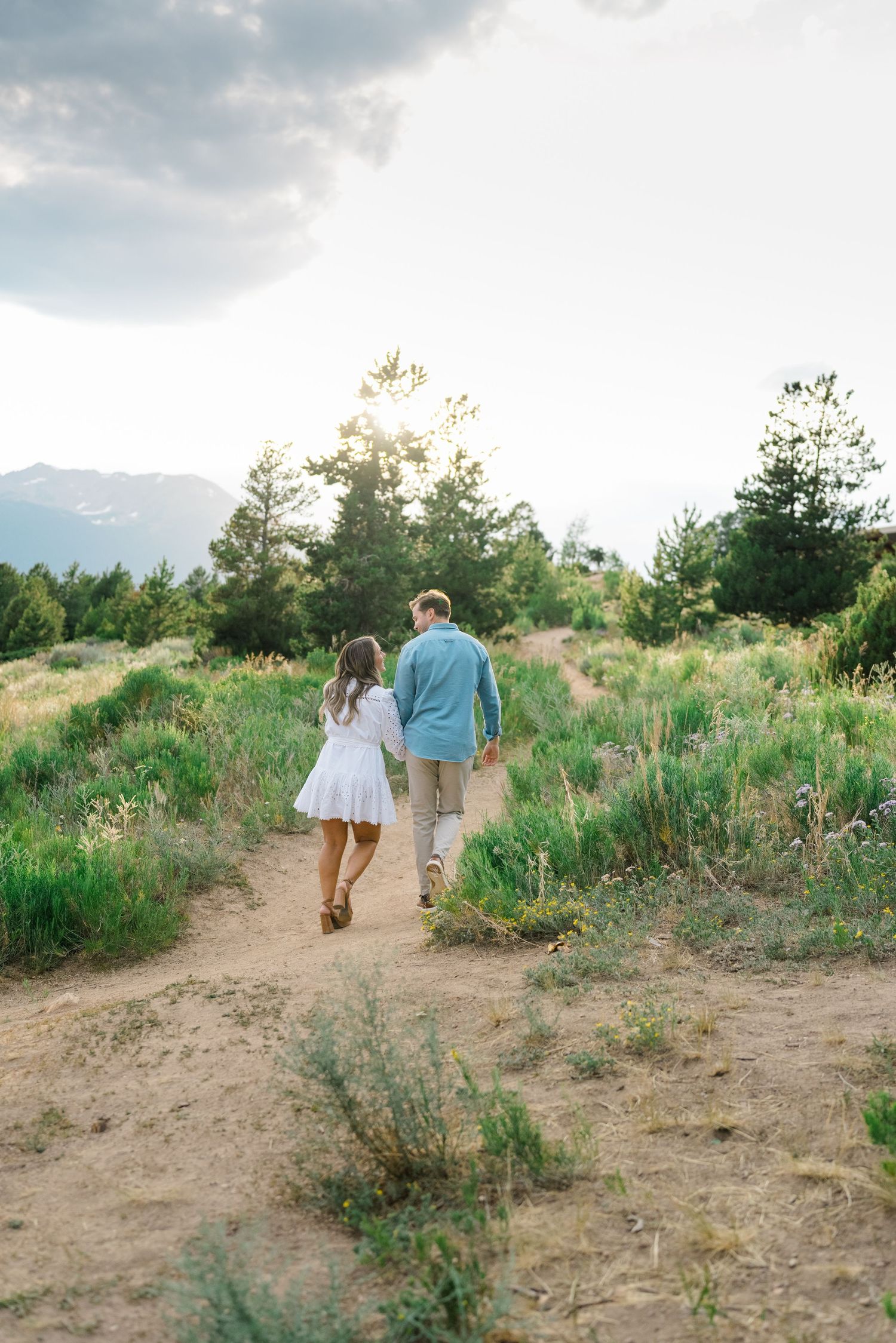 A couple walks hand in hand along a winding dirt path through desert brush and wildflowers at sunset at lake dillon.