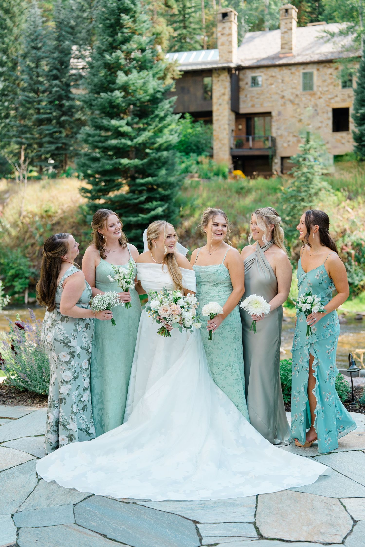 A wedding party in mint green bridesmaid dresses poses together on a stone patio with mountain scenery in the background during vail wedding