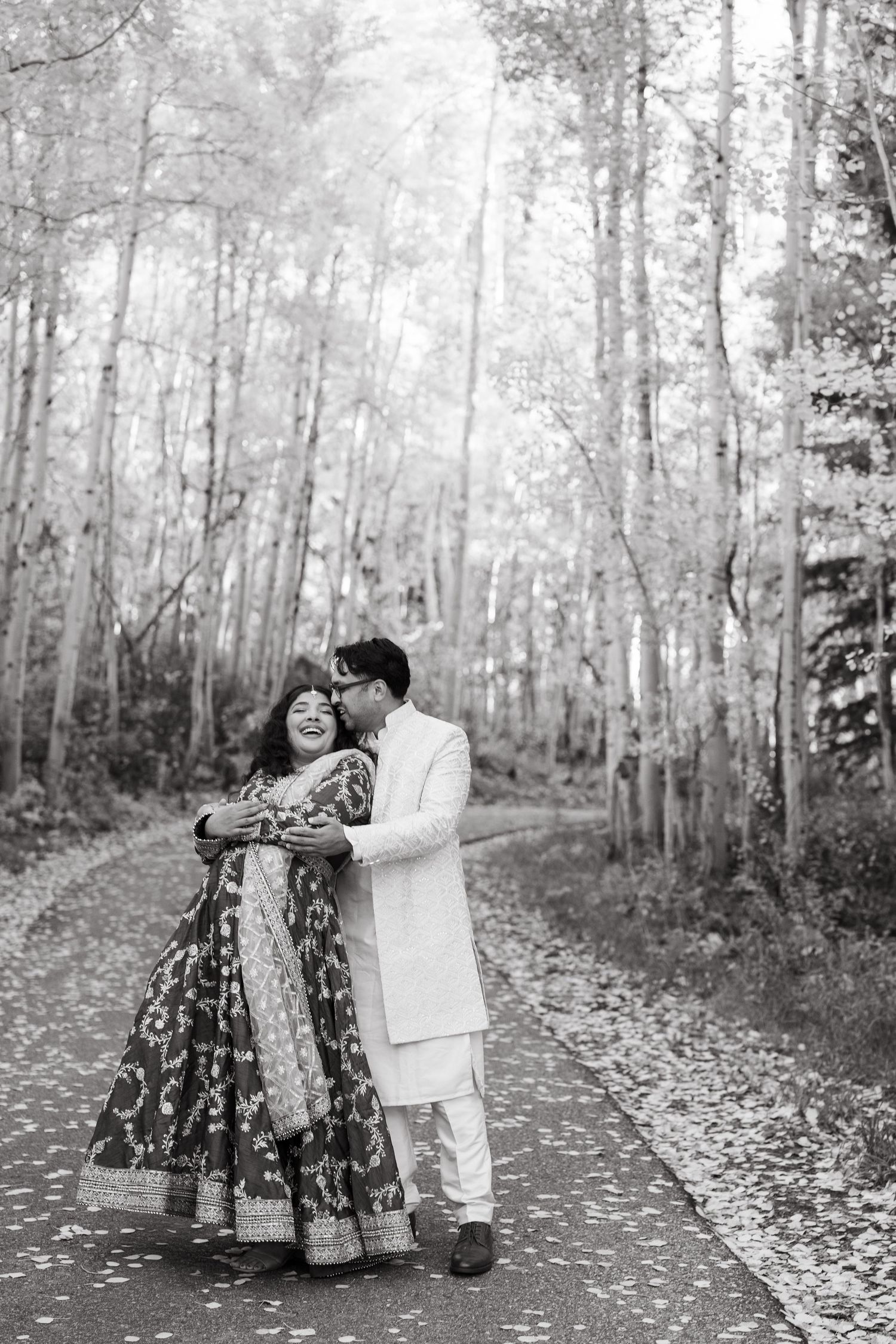 A couple in traditional attire shares romantic moments on a leaf-covered path in an autumn aspen forest.