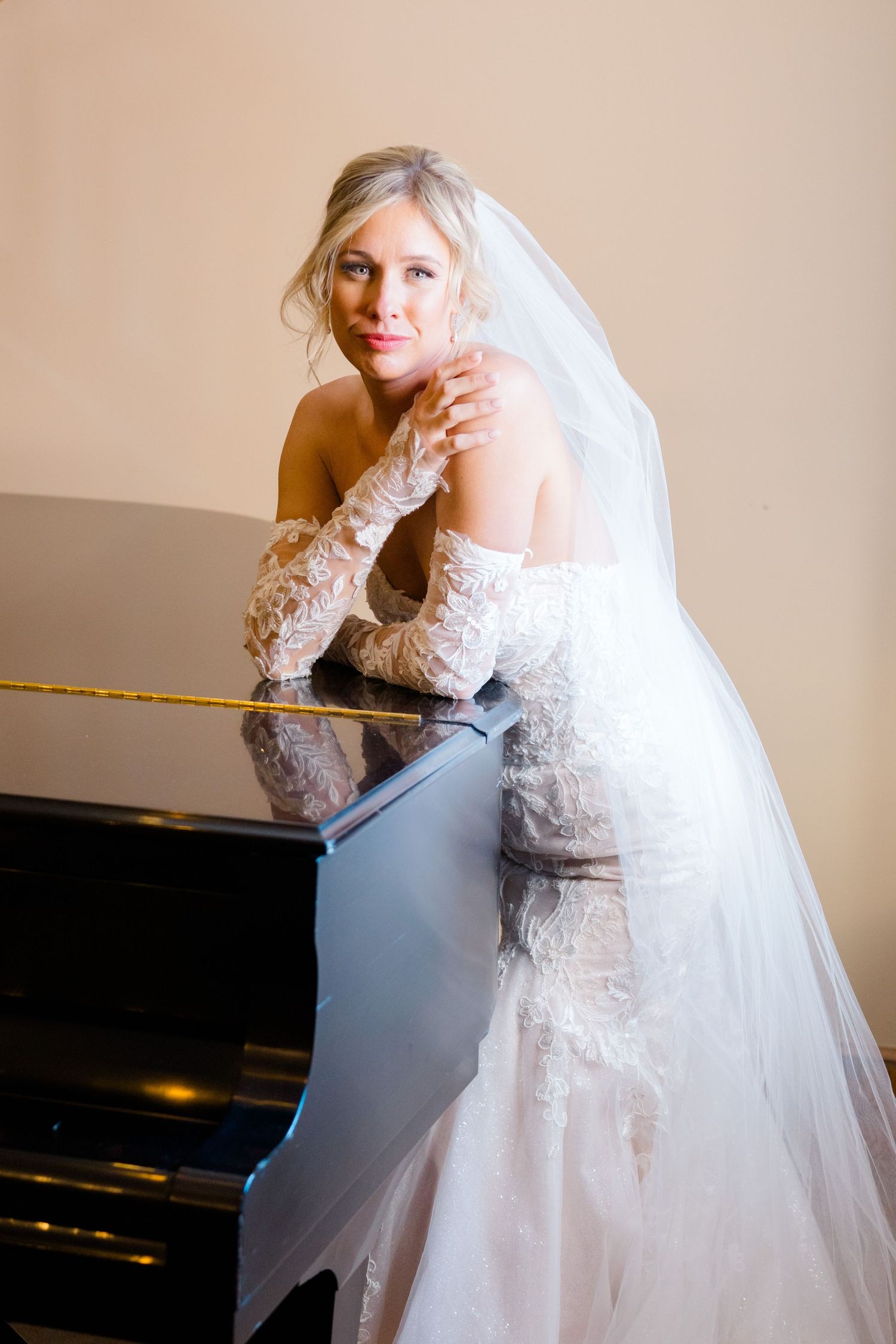 bride posing on the piano with hands by face and veil draping over shoulder