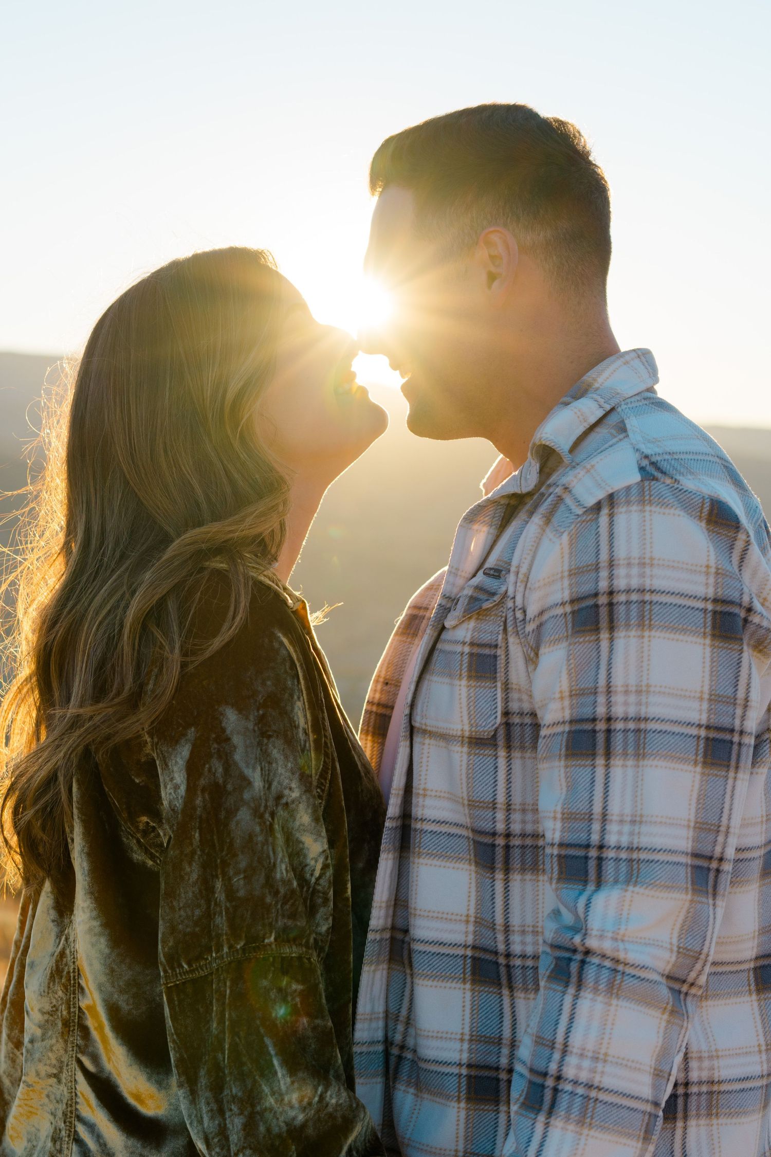 A couple in silhouette shares a romantic moment at sunset, with golden light streaming through their profiles.