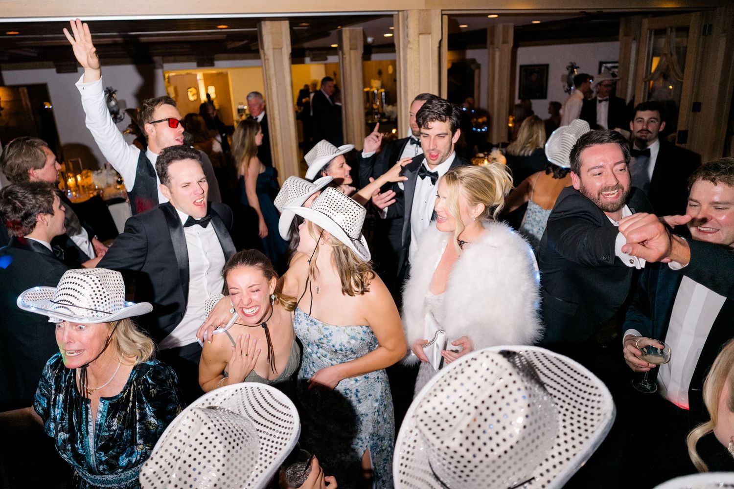 Lively wedding reception dance floor with guests in formal wear and white cowboy hats celebrating together.