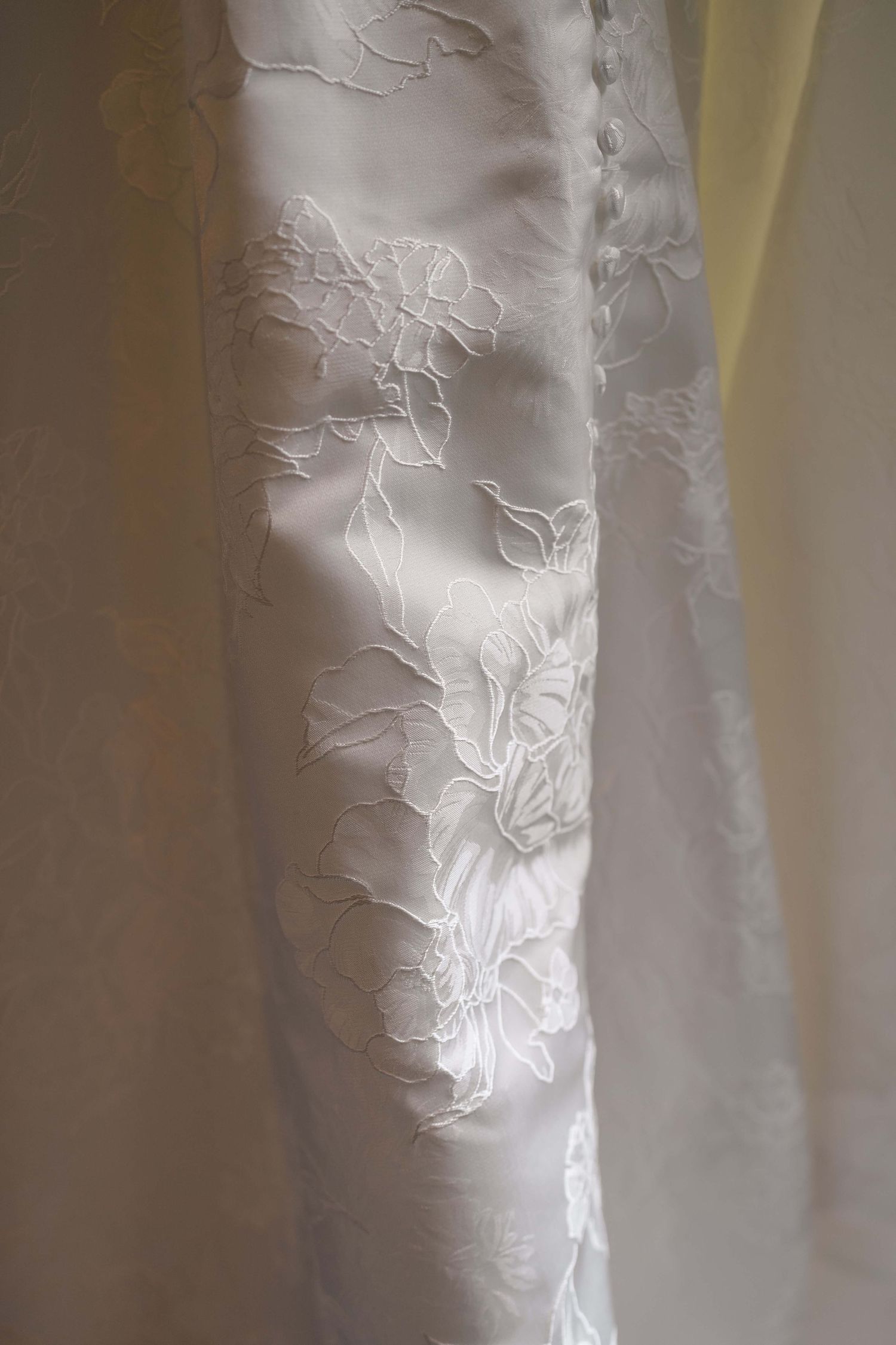 Close-up of elegant white wedding dress fabric featuring delicate floral lace embroidery on satin.