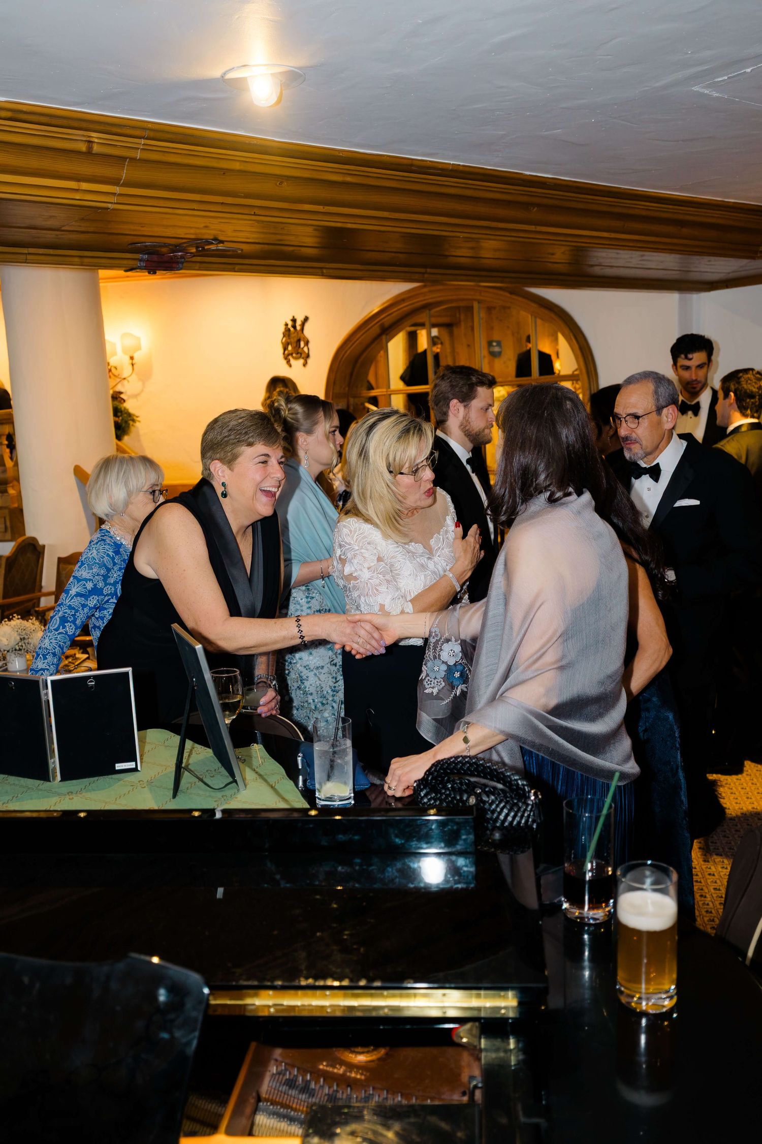 Elegantly dressed guests mingling and shaking hands at a formal evening event near a grand piano.