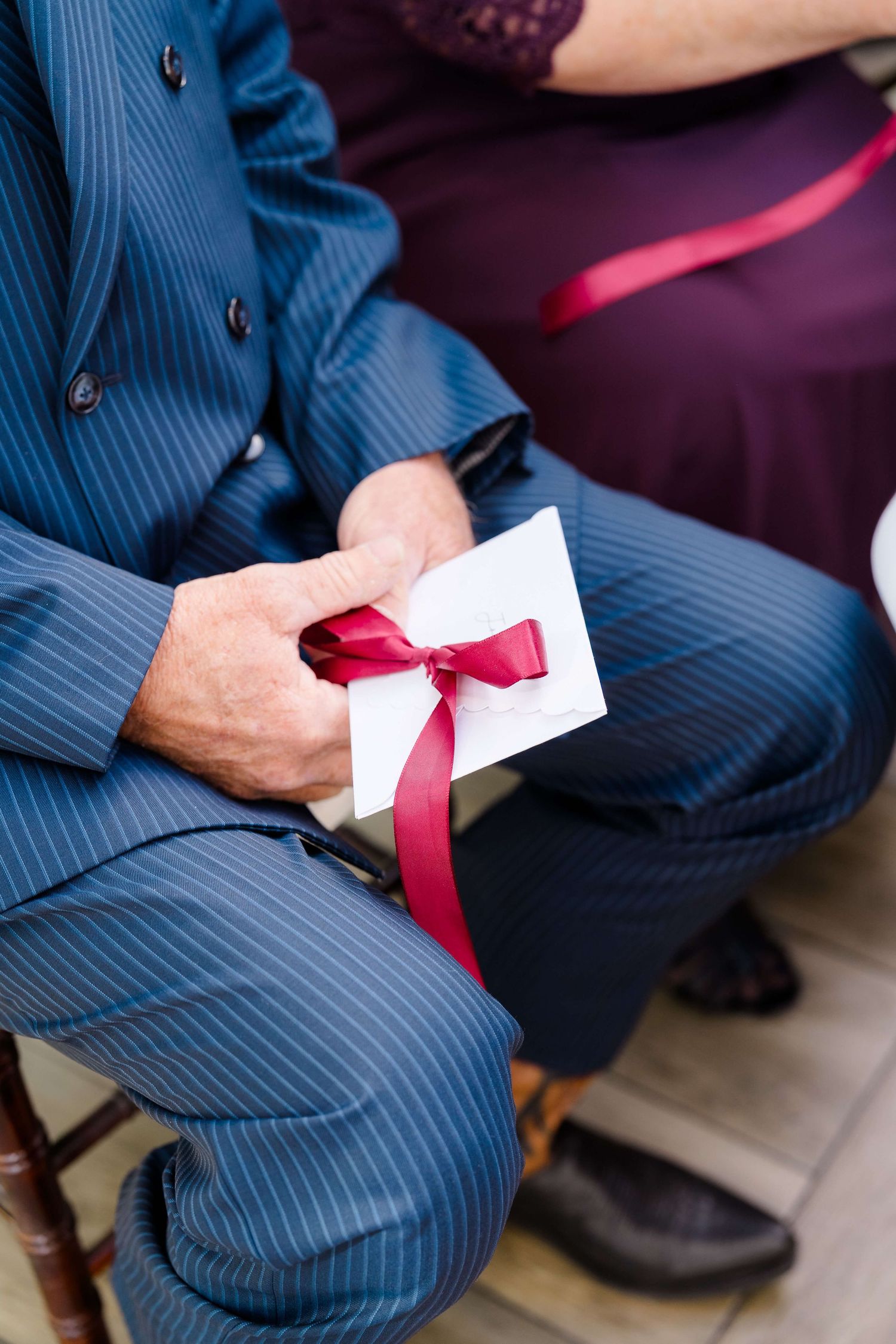 Man in blue pinstripe suit holding a white envelope tied with a red ribbon bow.