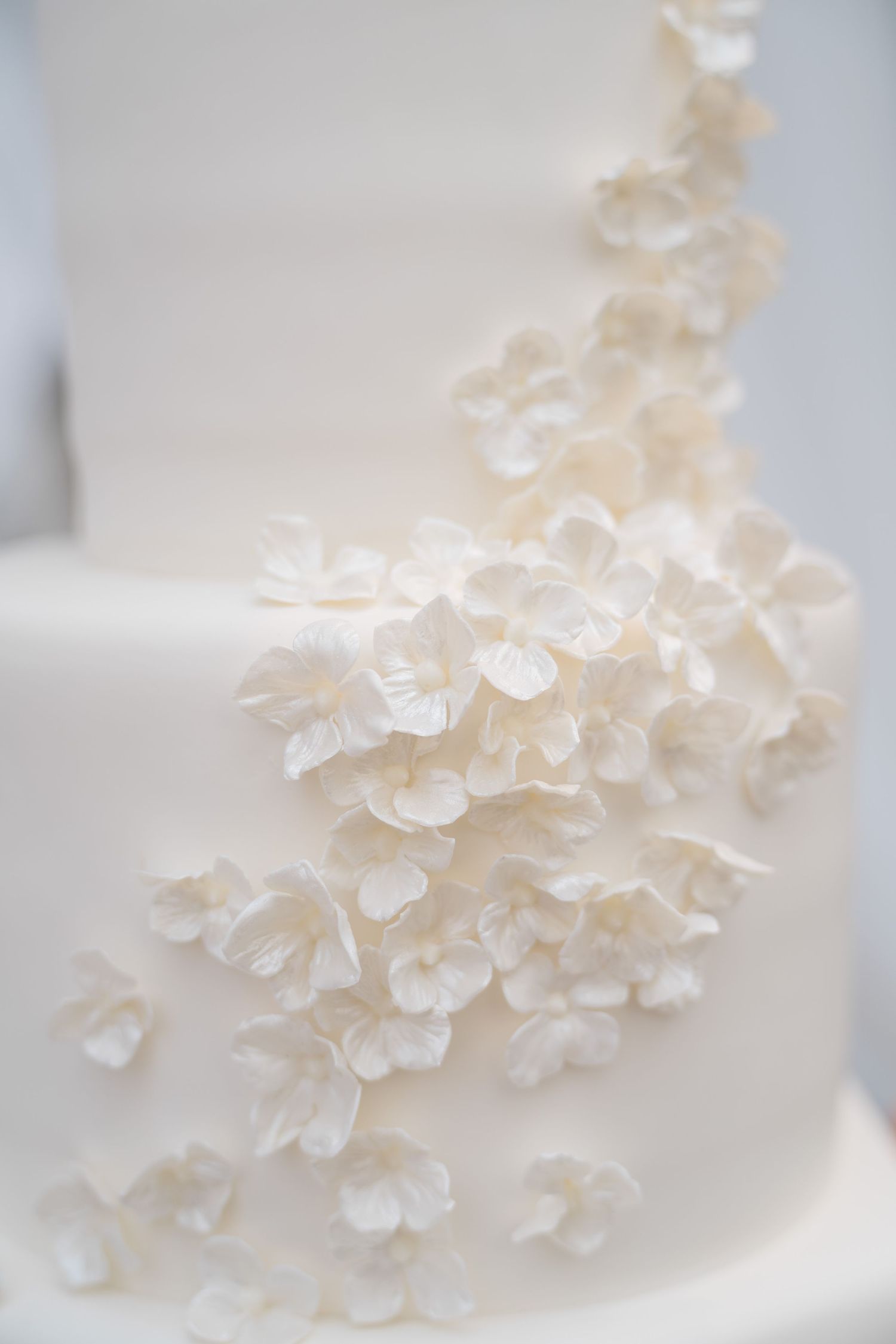 Elegant white wedding cake with delicate sugar flowers cascading down tiers, close-up detail shot at arrabelle vail wedding