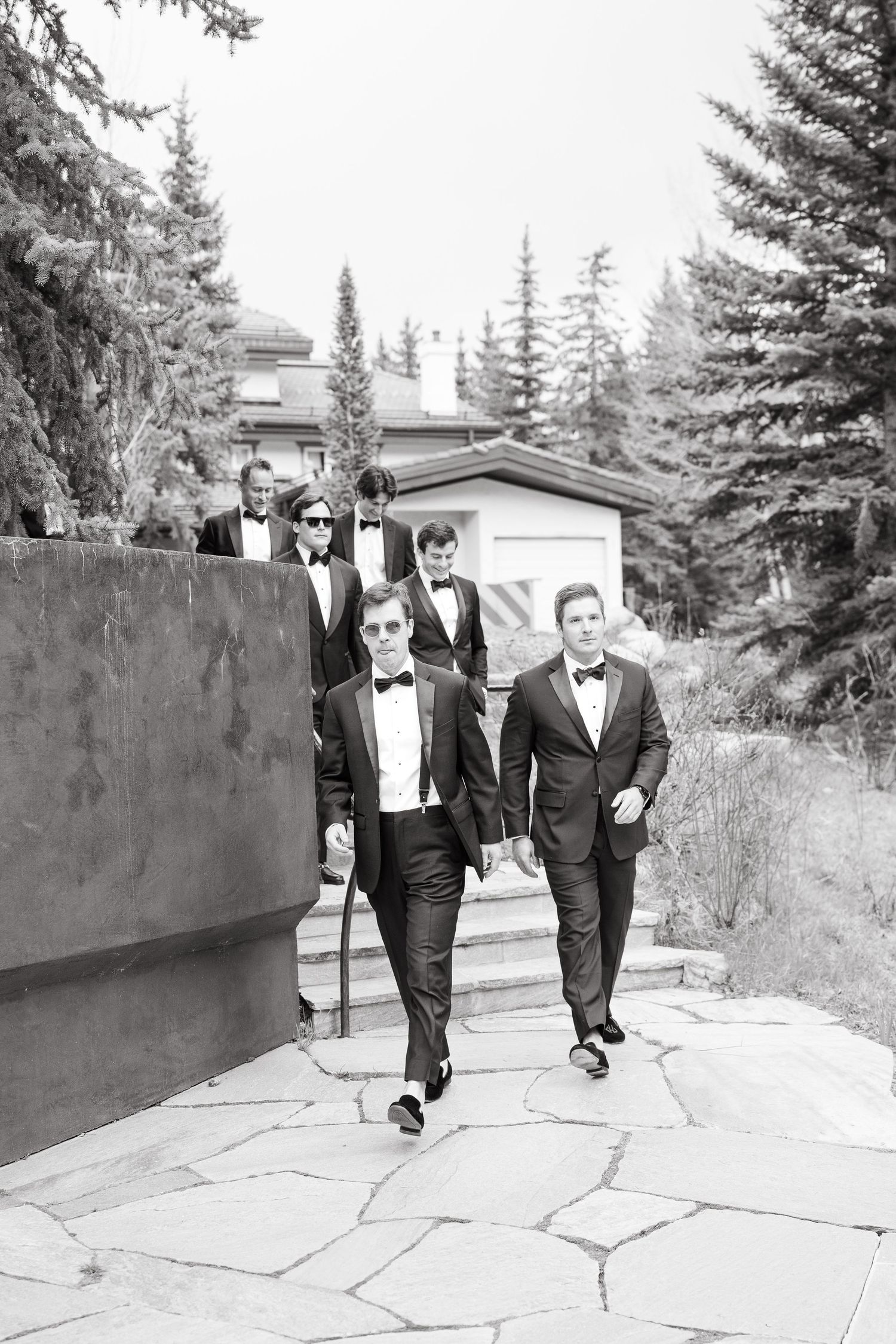Taken by Vail Wedding Photographer Black and white photo of groomsmen in tuxedos walking confidently down a stone path.