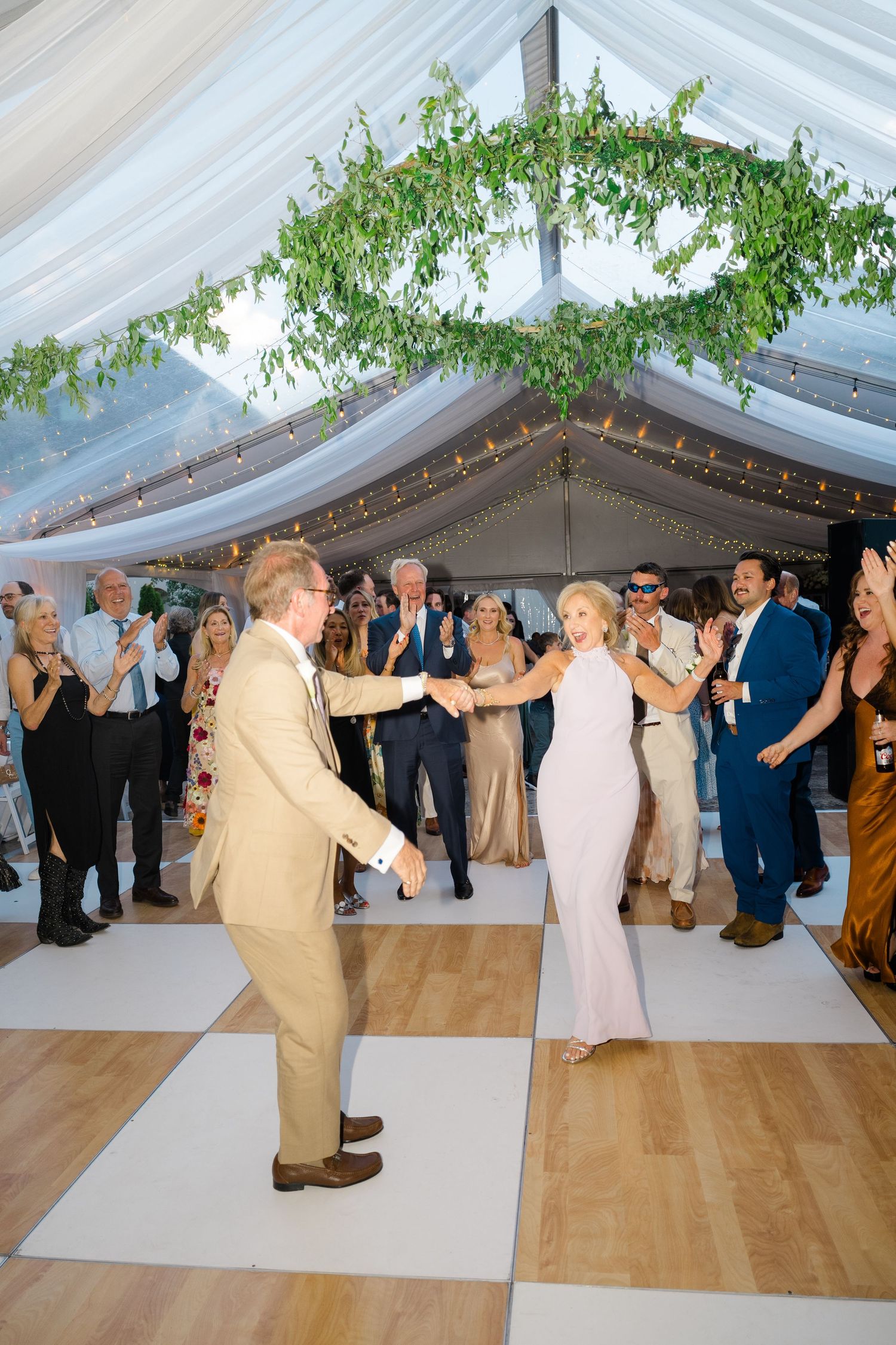 Couple shares first dance at elegant wedding reception under draped tent with greenery and string lights.