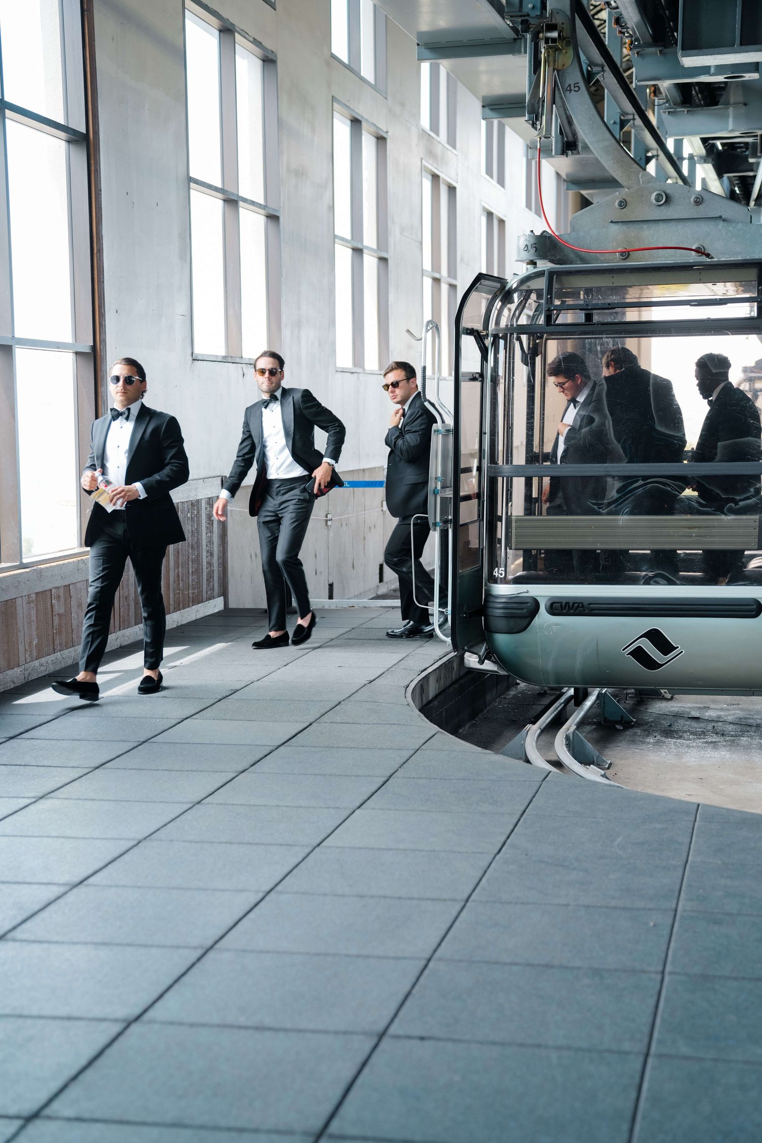 Groomsmen in black tuxedos and sunglasses pose near a ski gondola lift station to go to the vail mountain wedding deck