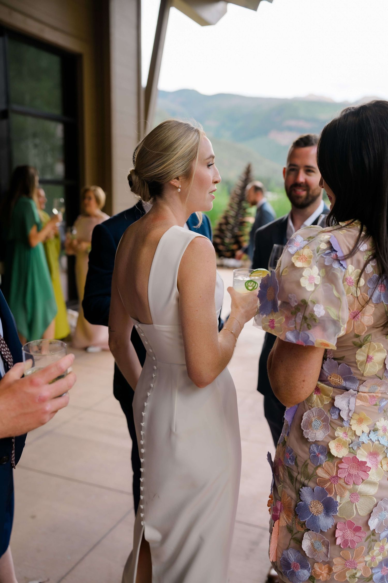 At Vail Golf Club Wedding Venue - Bride in elegant backless white gown socializing with guests at an outdoor wedding reception.