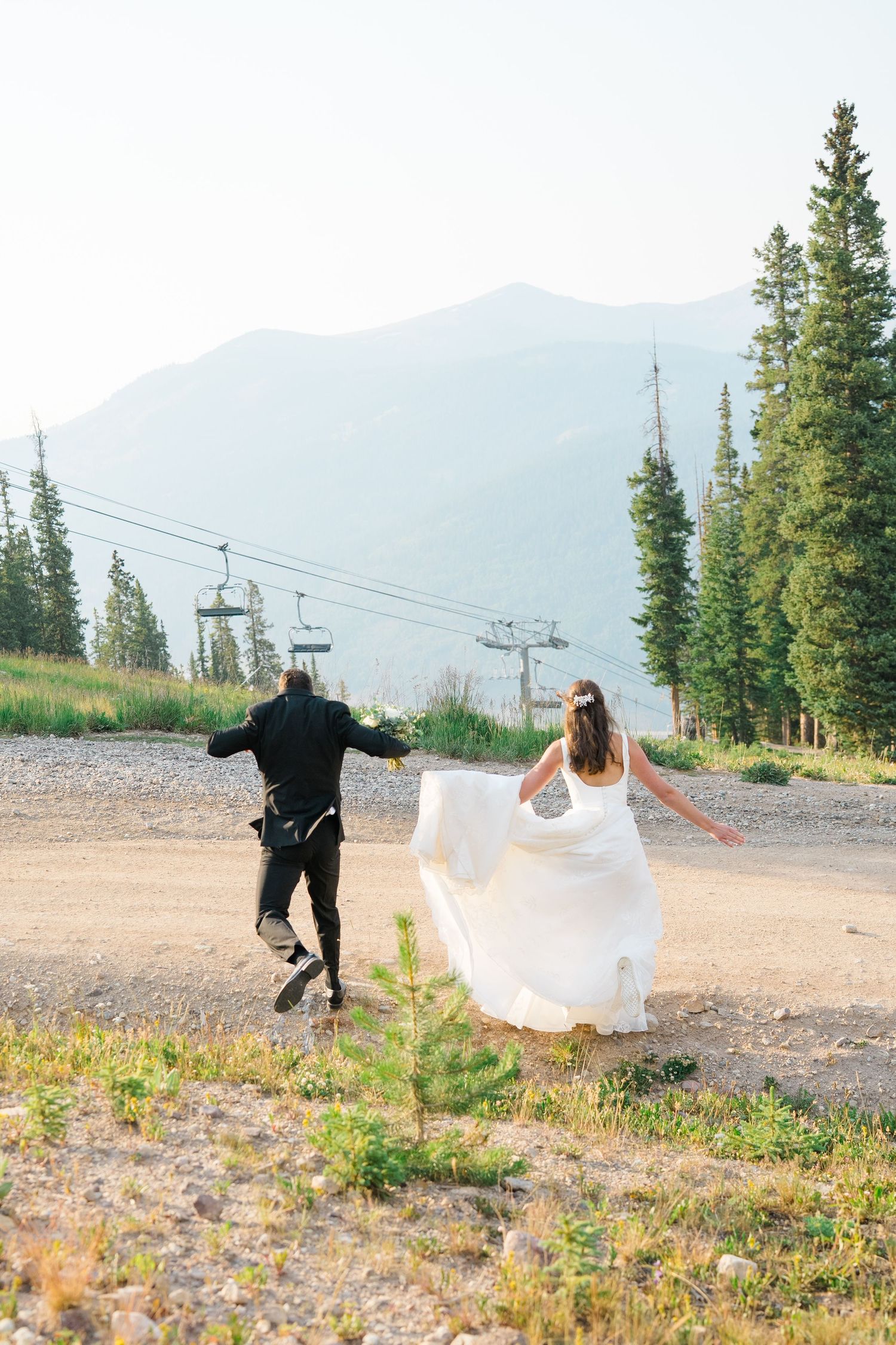 A wedding couple poses in a mountain meadow at copper mountain with ski lifts and evergreen trees in the background.
