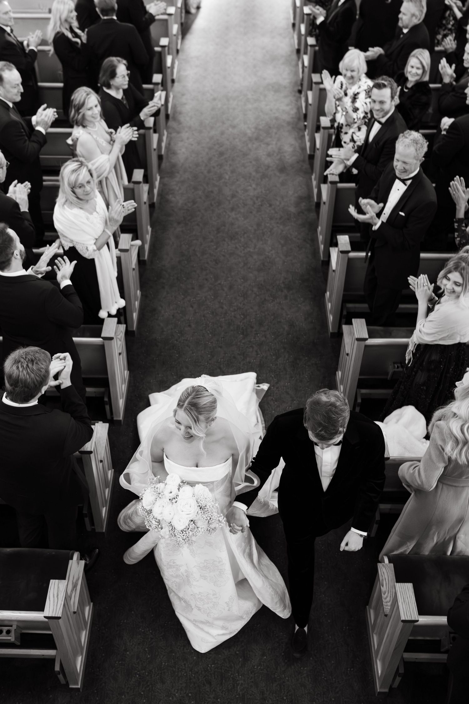Black and white aerial view of bride and groom walking down church aisle while guests applaud at wedding ceremony at Vail Sonnenalp Wedding.