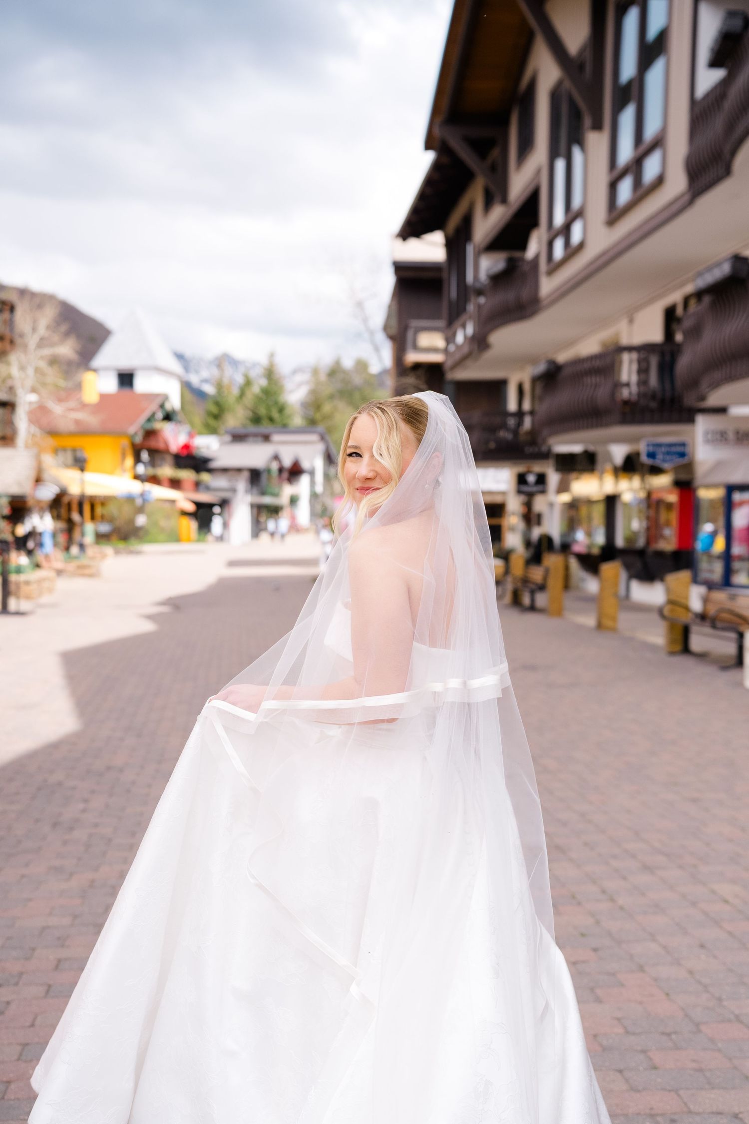 Smiling bride in white wedding dress and veil walks through a charming European-style village street on a sunny day at Vail Sonnenalp.