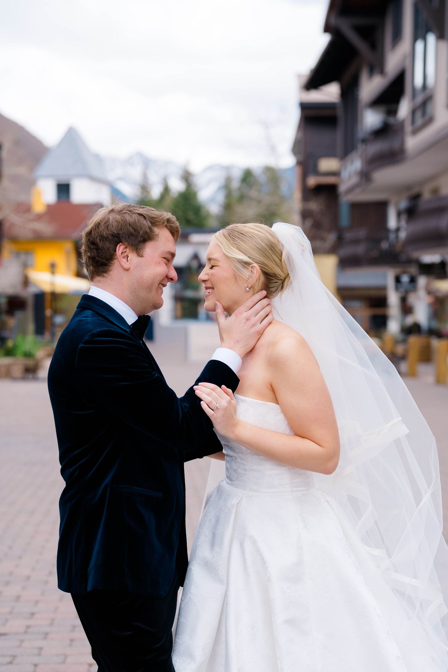 Bride and groom share a romantic moment outdoors in a mountain village, with the bride in a white gown and veil.