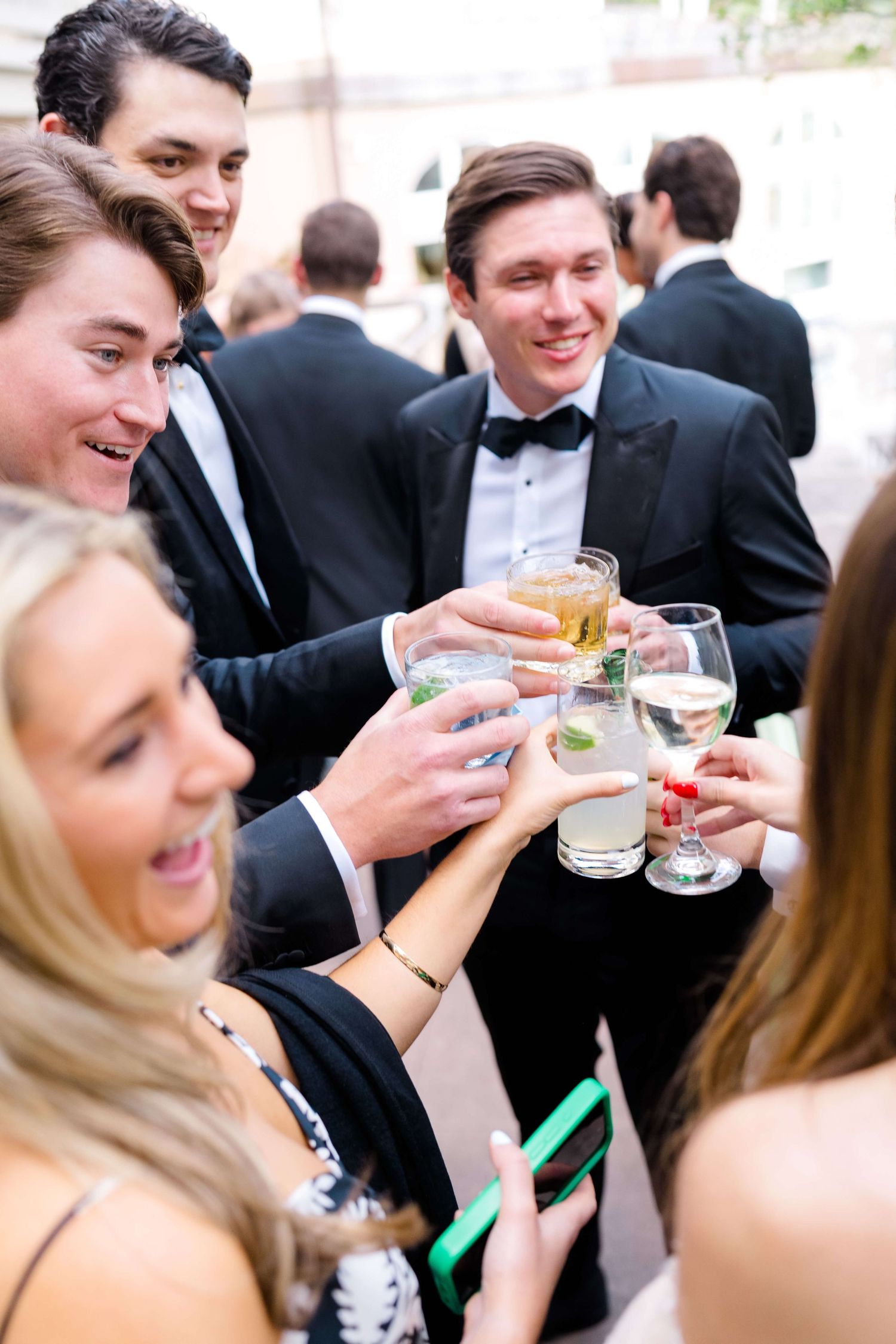 Elegantly dressed guests in black tie attire clinking cocktail glasses at a formal event.