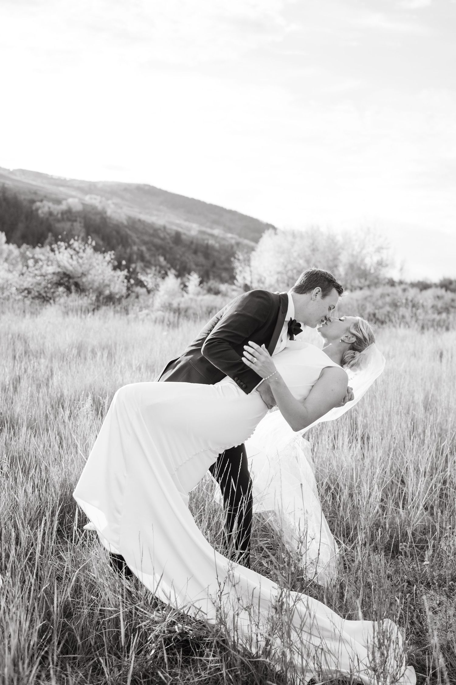 Romantic black and white wedding photo sequence of couple dipping in grassy meadow.