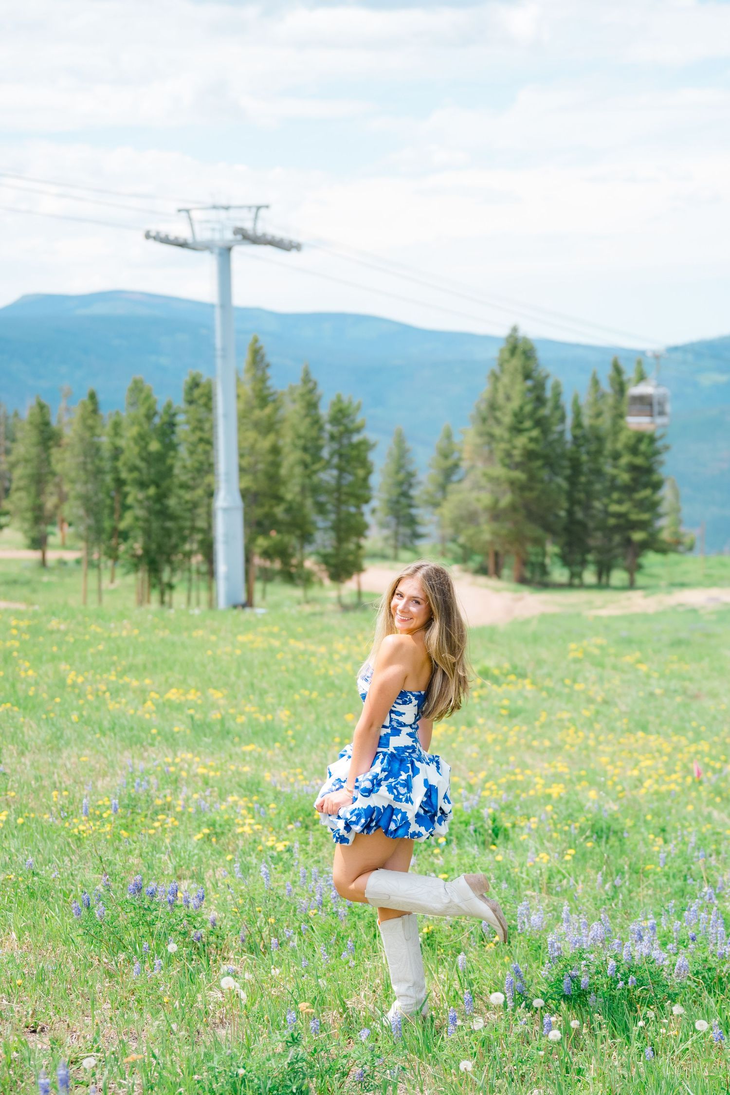 A blue floral dress twirls in a wildflower meadow near a ski lift in the mountains during vail senior photography session.