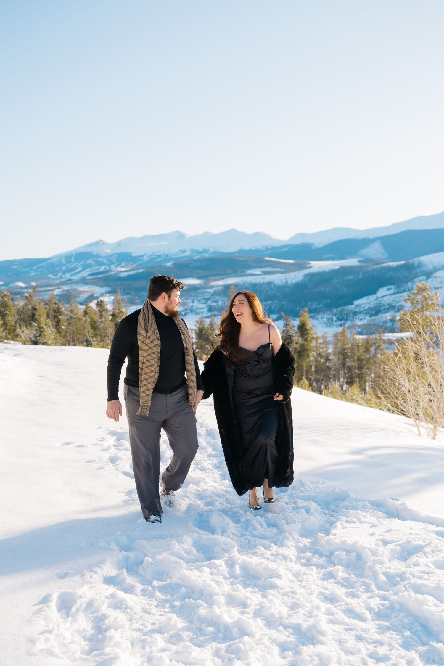 Two people playfully running and frolicking together in deep snow with scenic mountain views in the background.