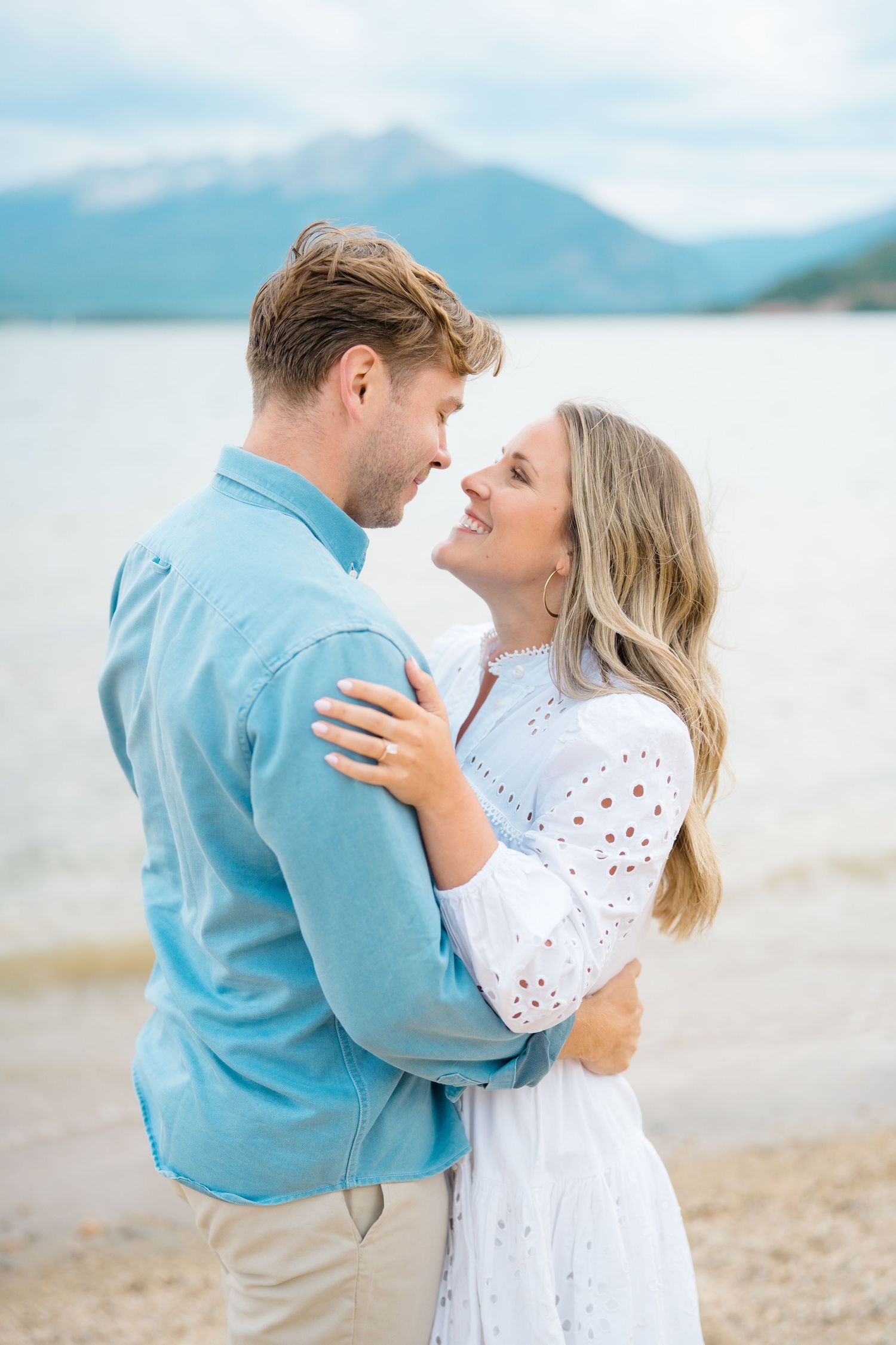 A romantic couple embraces on a scenic beach with mountains in the background.