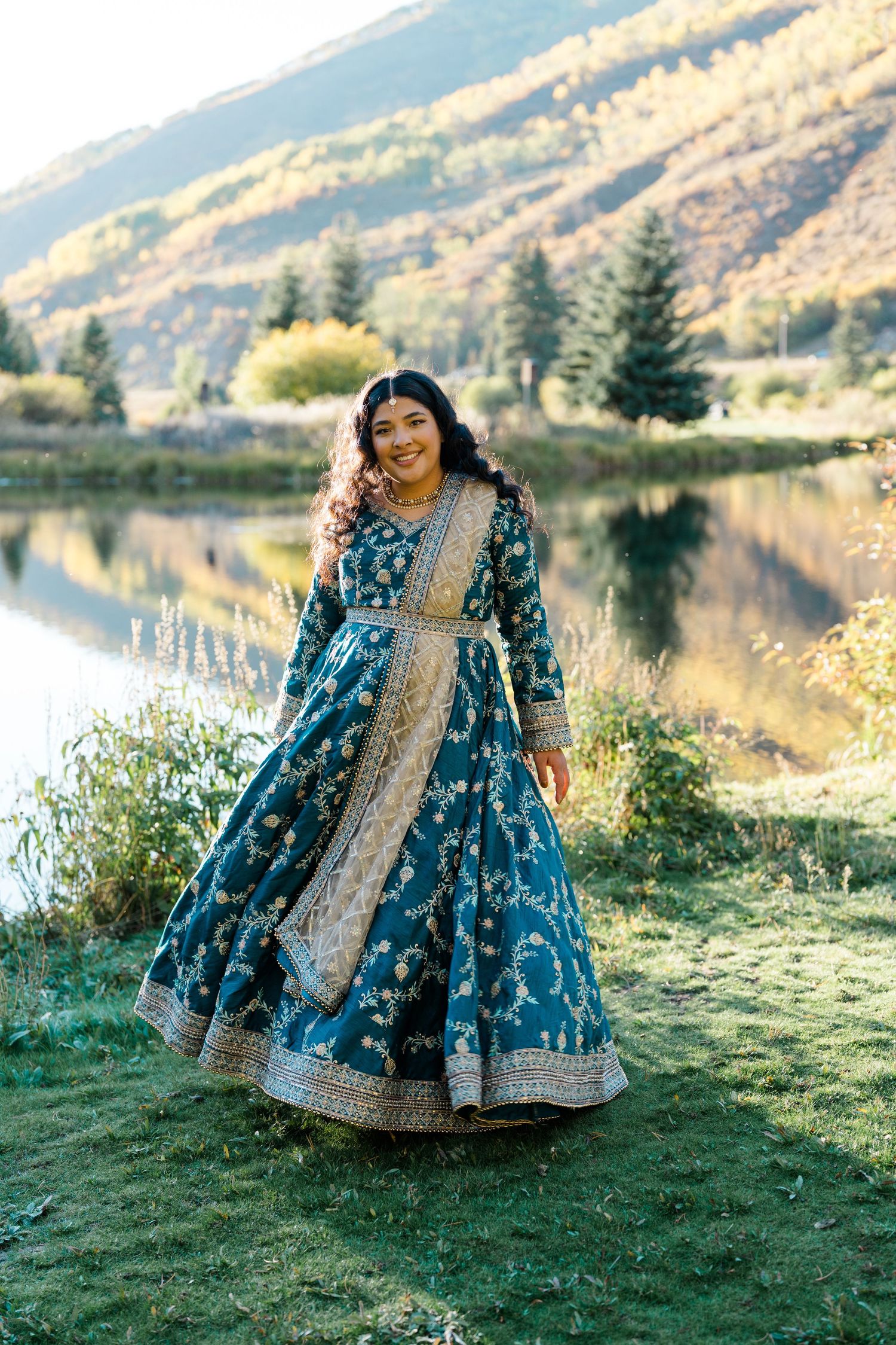 A flowing blue dress twirls gracefully against a scenic mountain lake backdrop during a photoshoot.