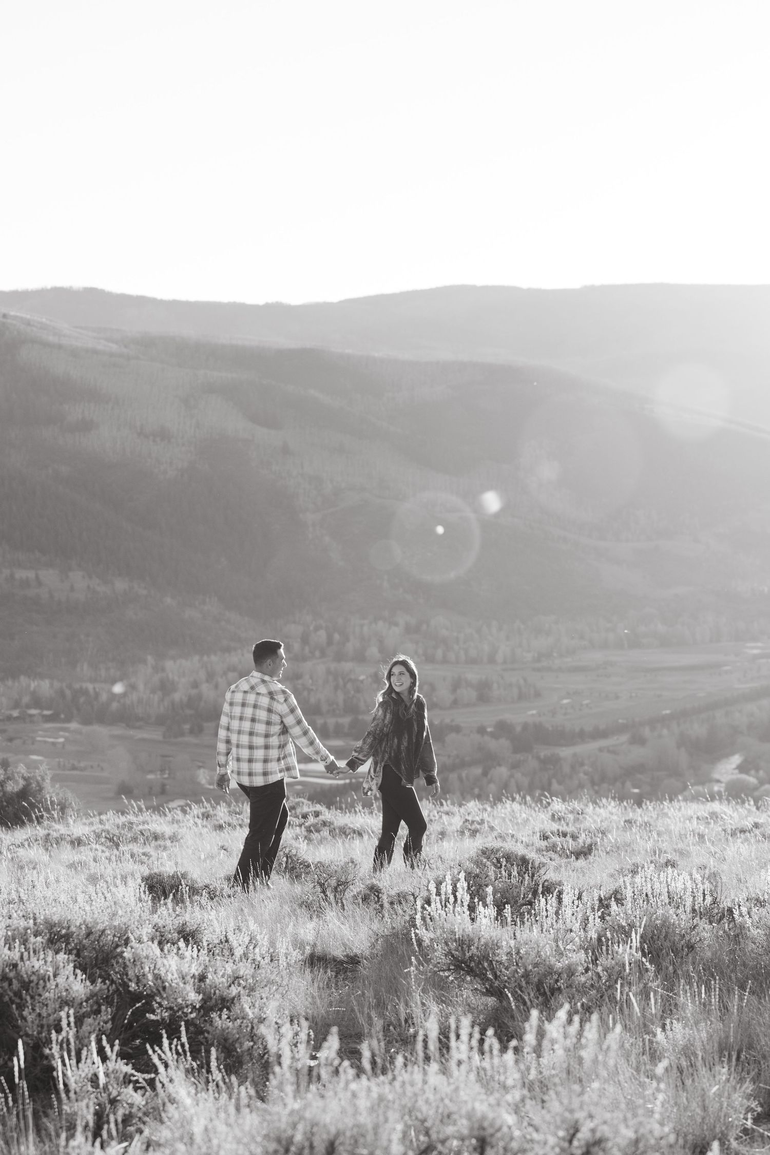 Couple walking together through a misty mountain meadow at sunset in black and white photography.