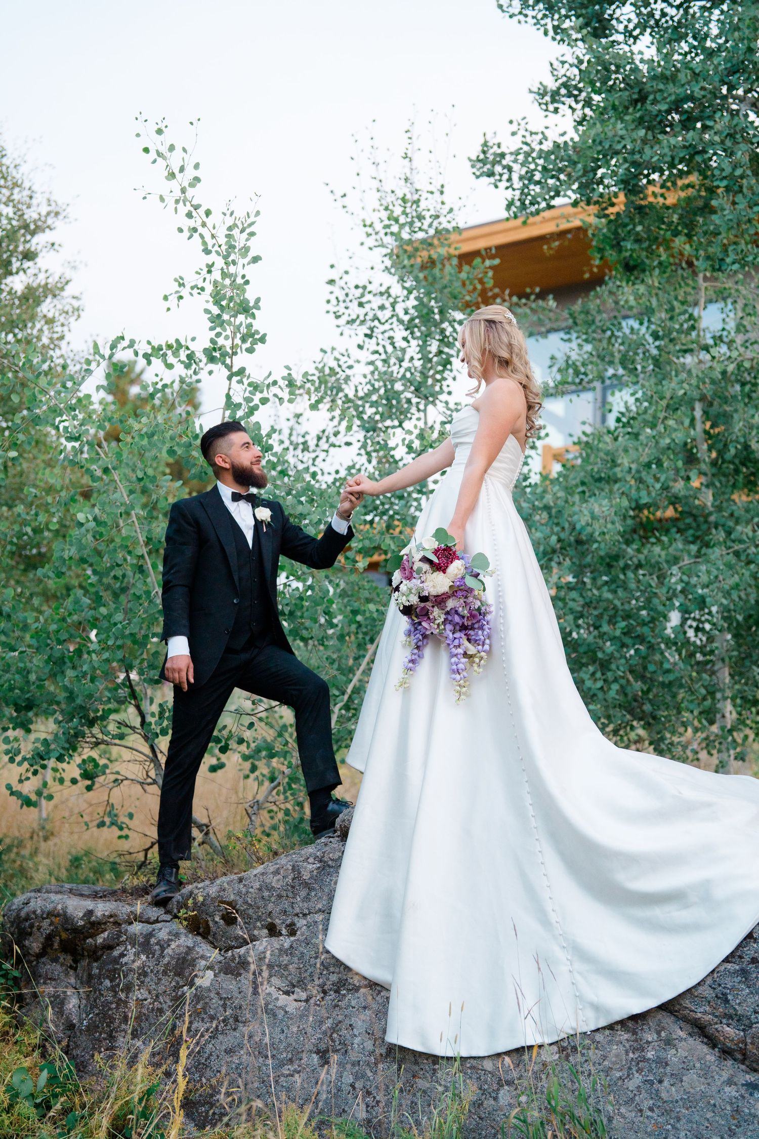 Newlywed couple dances playfully on a hillside surrounded by green trees during their wedding photoshoot during their Breckenridge wedding.