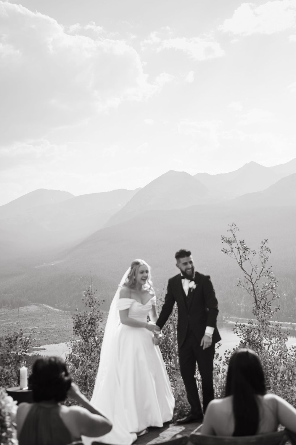 A scenic mountain wedding ceremony with attendees silhouetted against a dramatic cloudy sky and mountain backdrop during vail elopement.