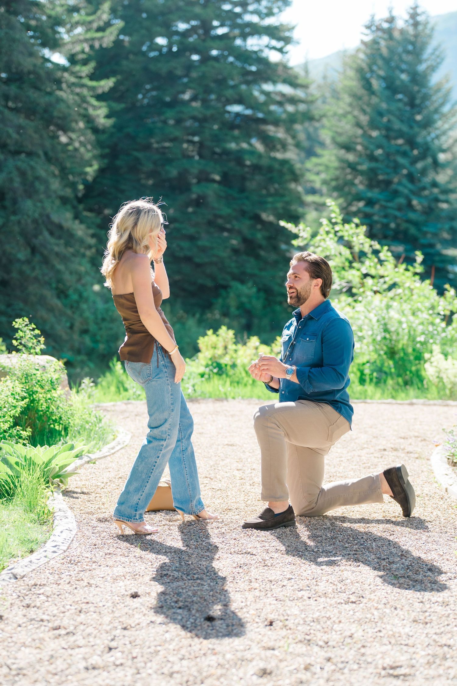 A couple shares a romantic moment on a dirt path surrounded by evergreen trees in a natural outdoor setting during vail proposal.