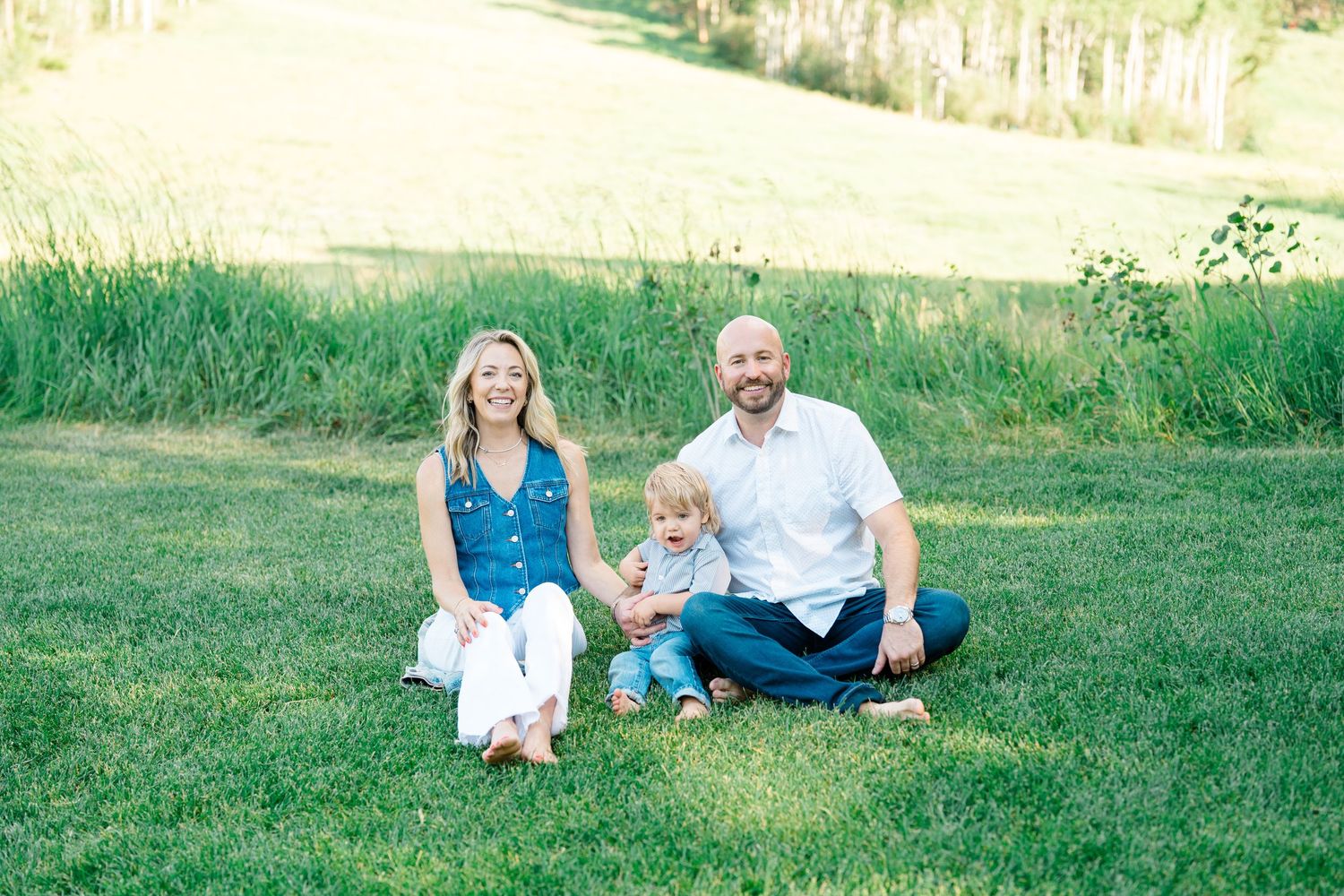 A family enjoys a candid moment together while sitting on green grass during a summer photoshoot.