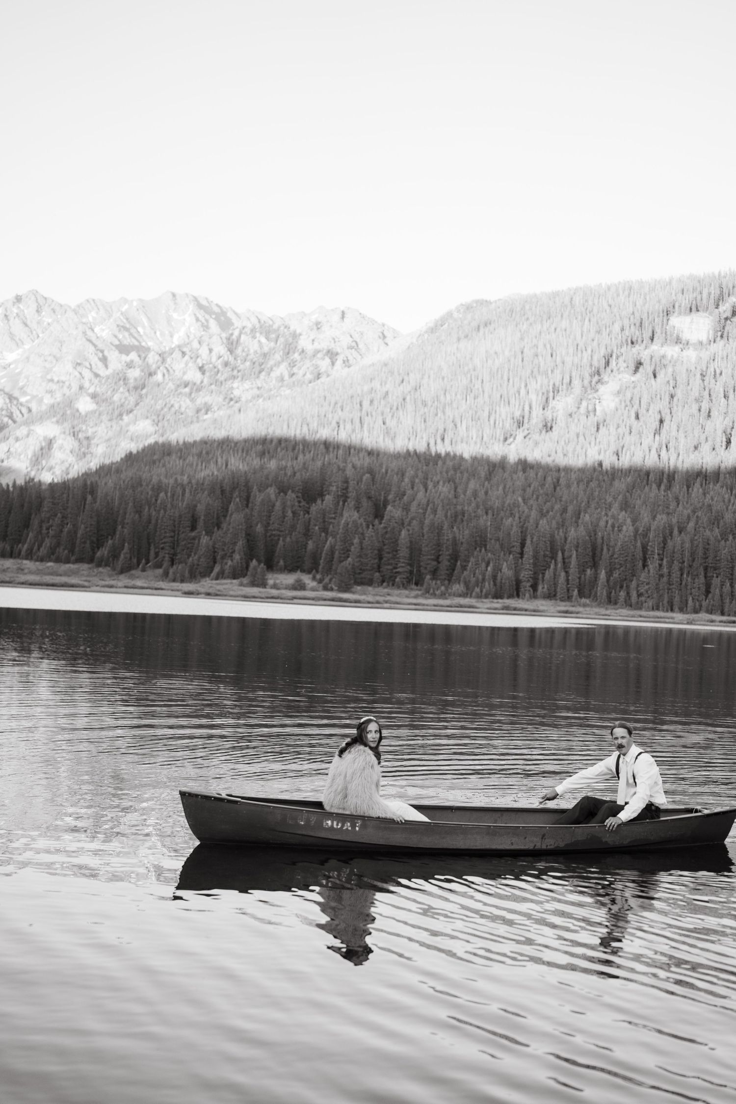 Black and white photo of canoes gliding across a serene mountain lake with evergreen forests in the background at Piney River Ranch.