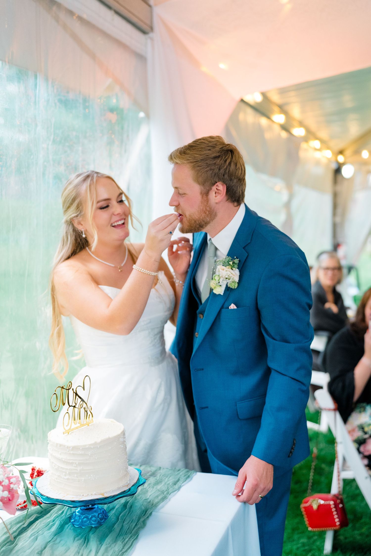 A joyful wedding cake cutting moment under a tent with string lights and decorative details.