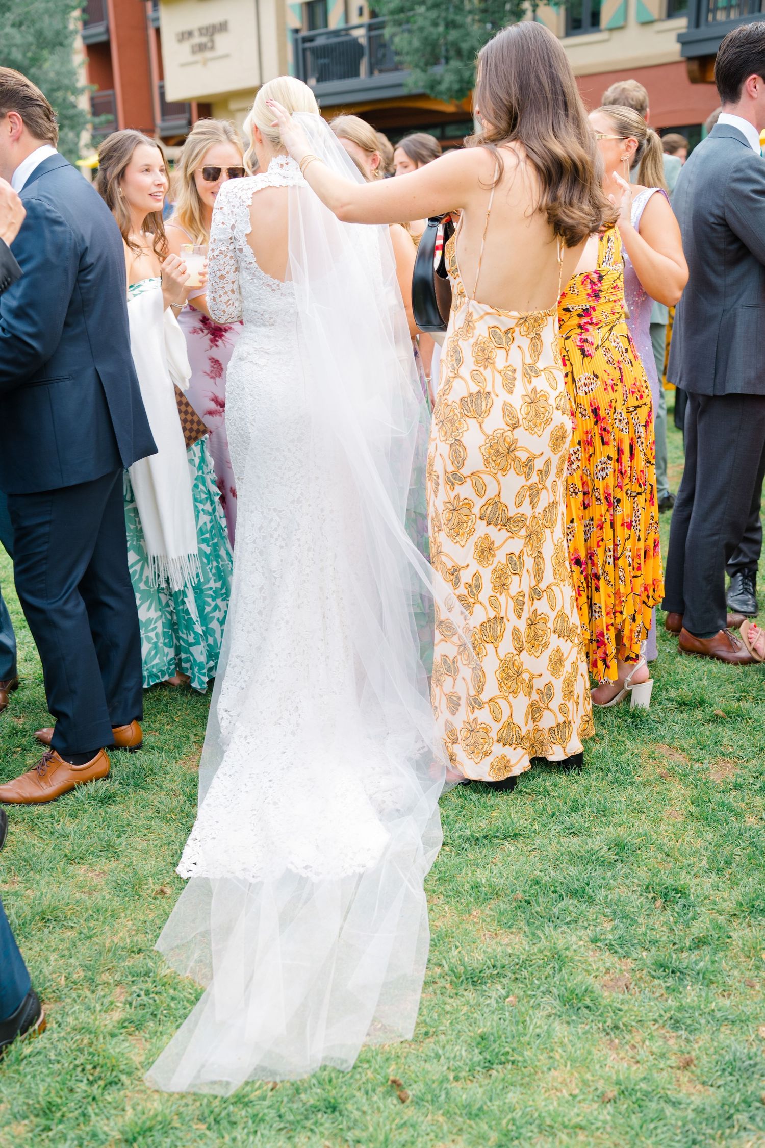 At Arrabelle Wedding Cocktail hour a bridesmaid adjusts the veil of a bride in a lace gown at an outdoor wedding reception.