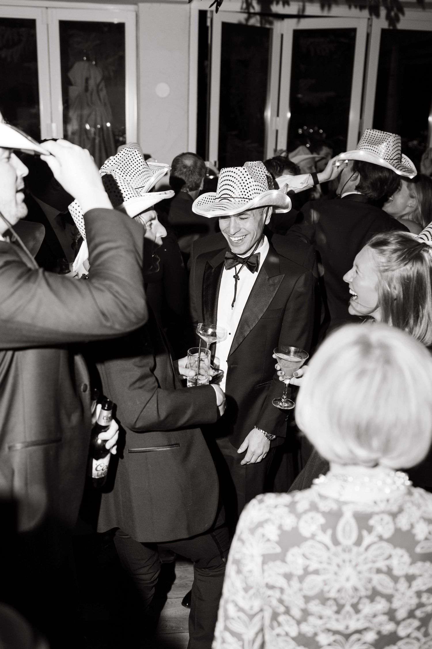 Black and white photo of wedding guests dancing and celebrating wearing striped cowboy hats at a lively reception party.