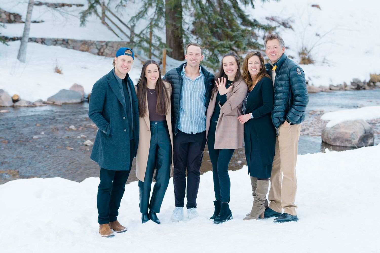 Family members gather for outdoor portraits in a snowy winter landscape with pine trees.